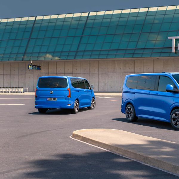 Два сини микробуса Volkswagen, паркирани пред терминал на летище с модерна стъклена фасада.