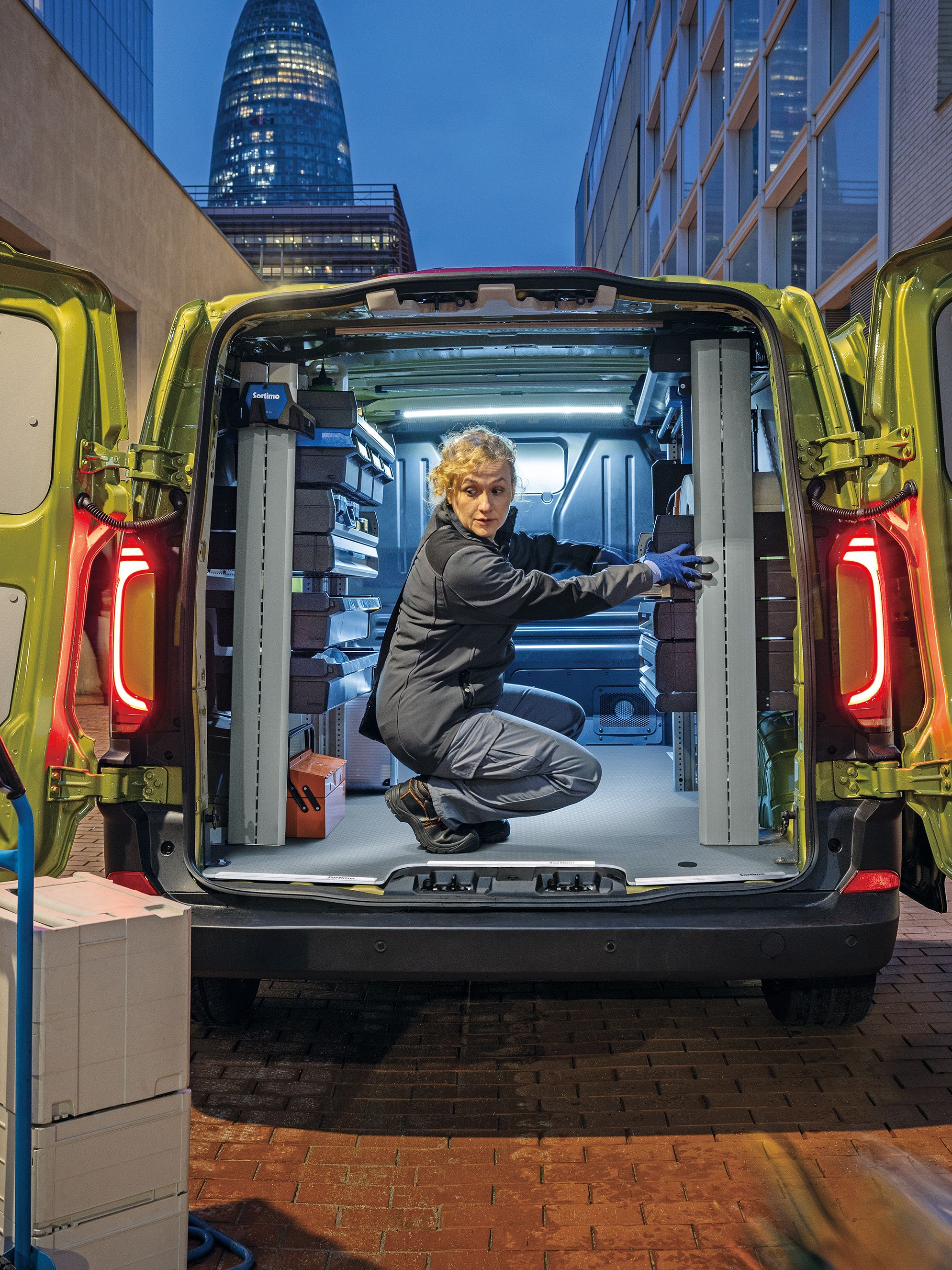Жена организира работно оборудване във Volkswagen Transporter с отворени задни врати на градска улица