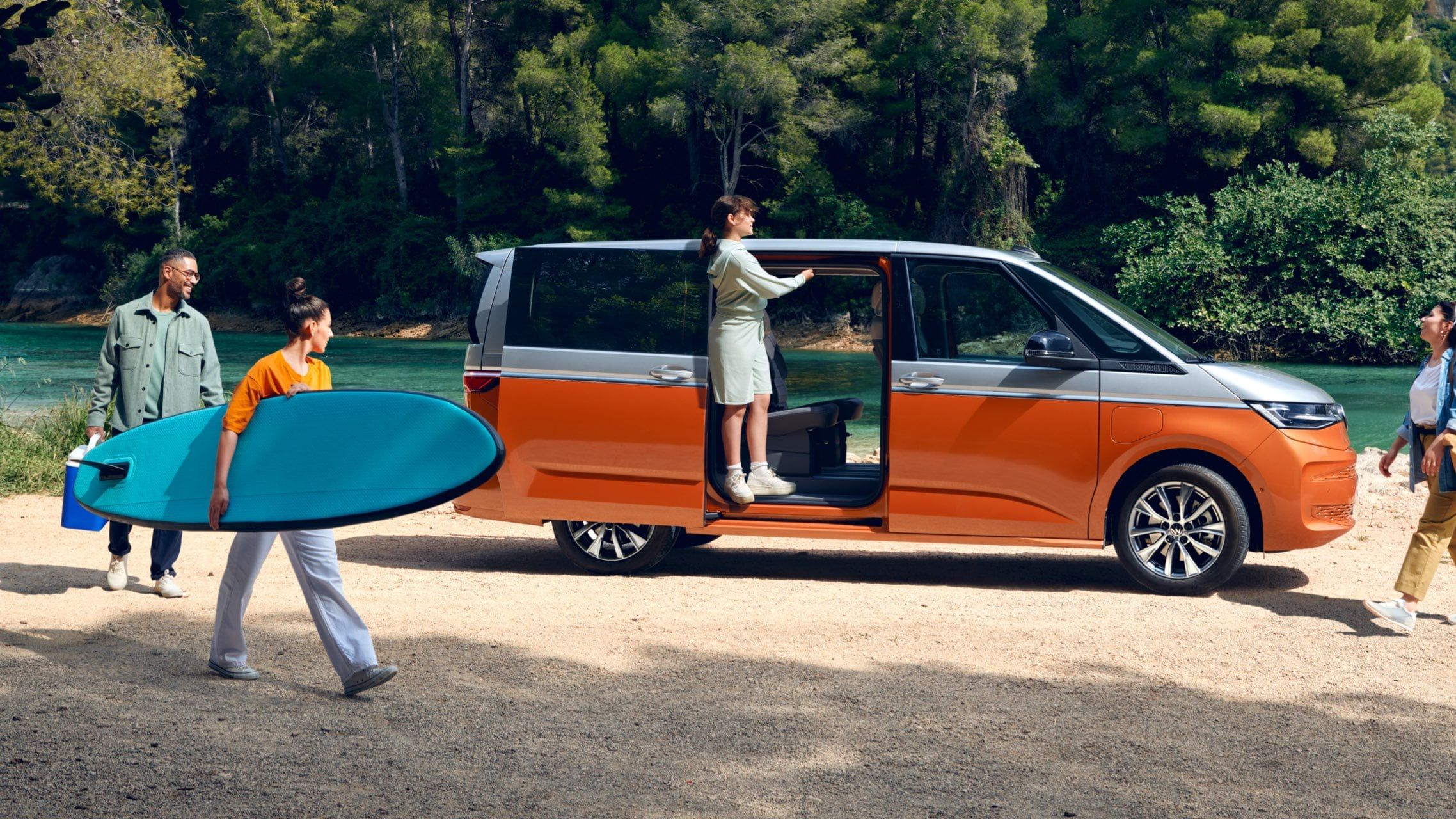 Ein neuer VW Multivan T7 2021 Energetic eHybrid parkt vor einem Fluss und Menschen laufen um ihn herum.