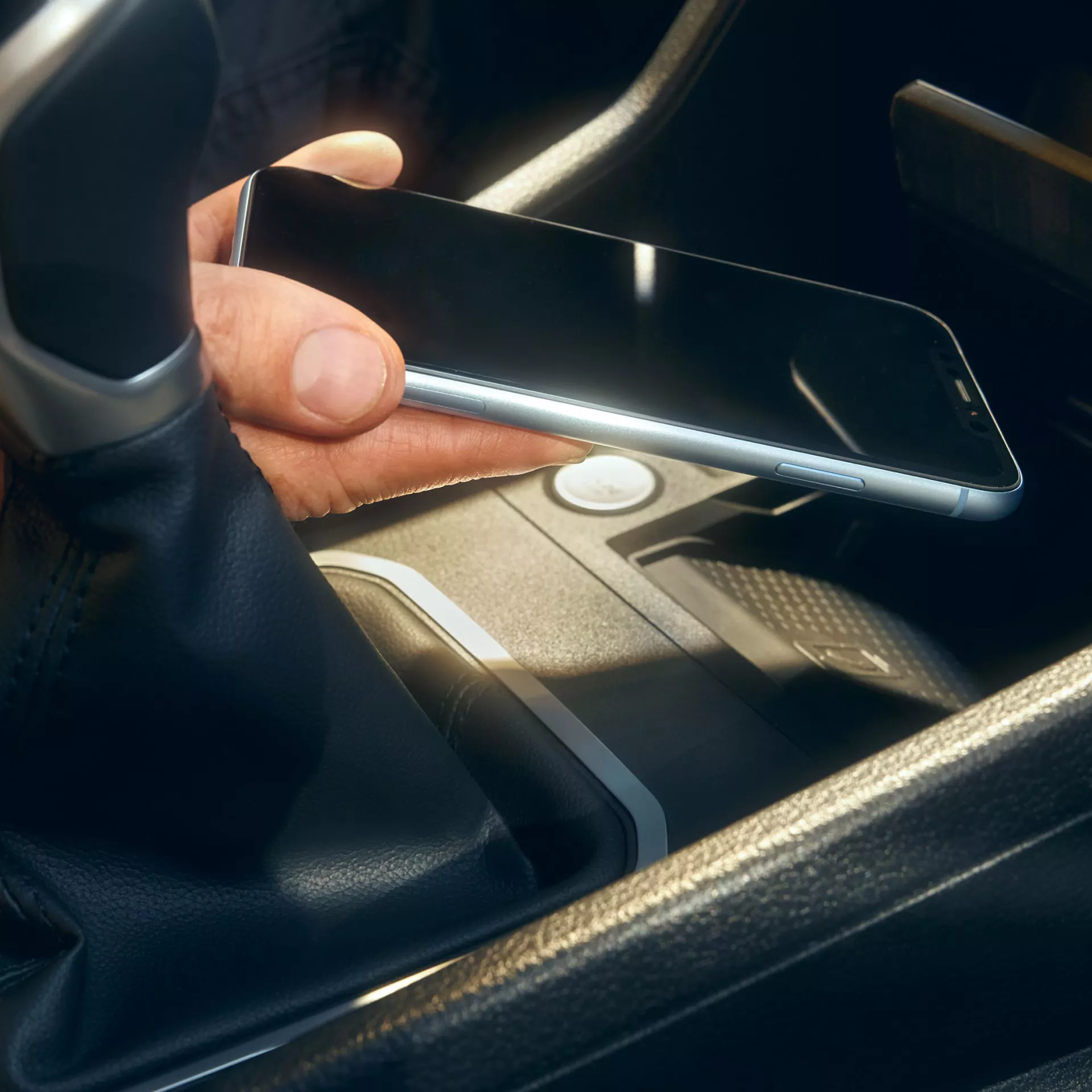 Ръка поставя смартфон върху безжично зарядно устройство в централната конзола на автомобил.