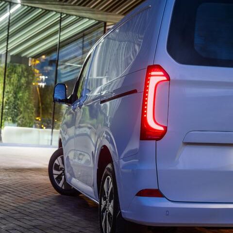 Задна част на новия Volkswagen e-Transporter, паркиран пред модерна офис сграда вечер.