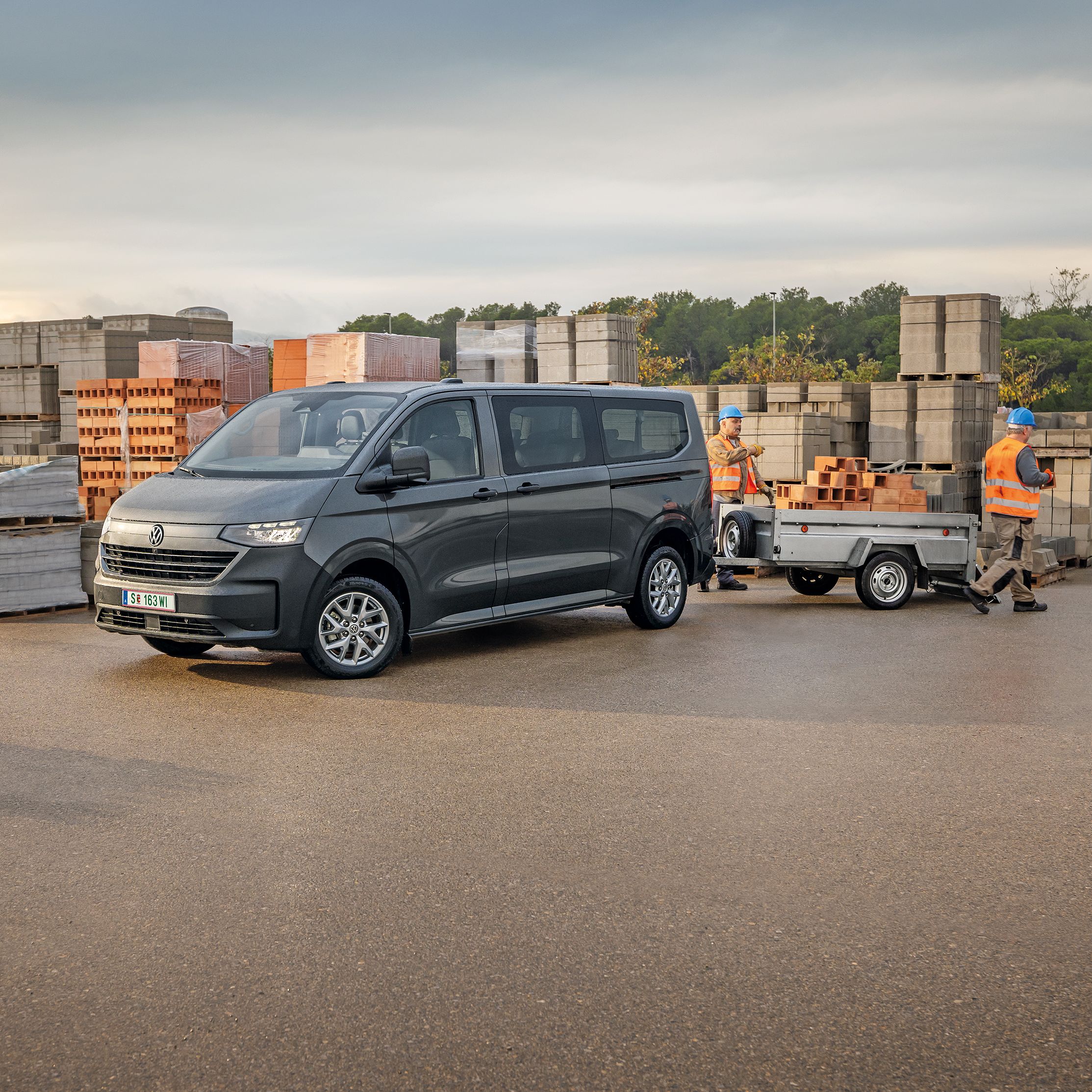 Volkswagen Transporter с ремарке на строителен обект до работници, които товарят тухли.