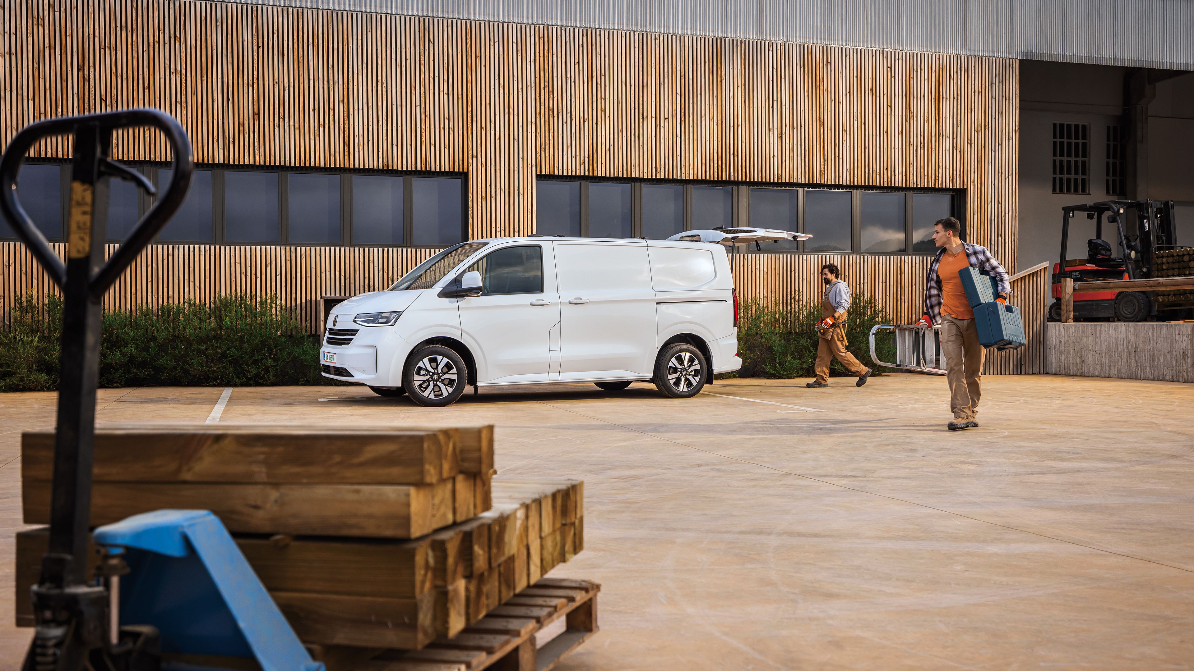 Електрически ван Volkswagen e-Transporter на строителен обект с двама работници, носещи инструменти и материали.