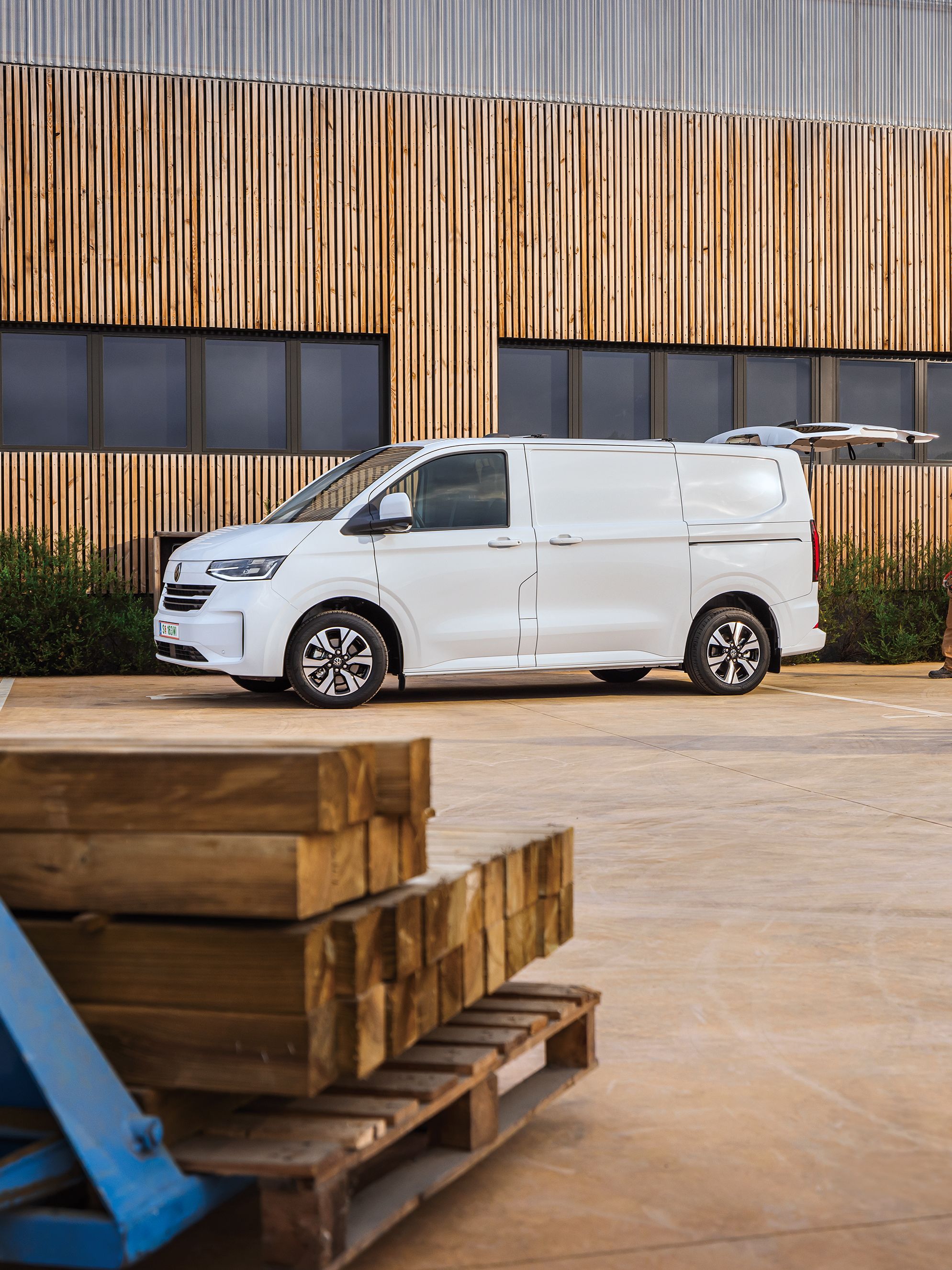 Електрически ван Volkswagen e-Transporter на строителен обект с двама работници, носещи инструменти и материали.