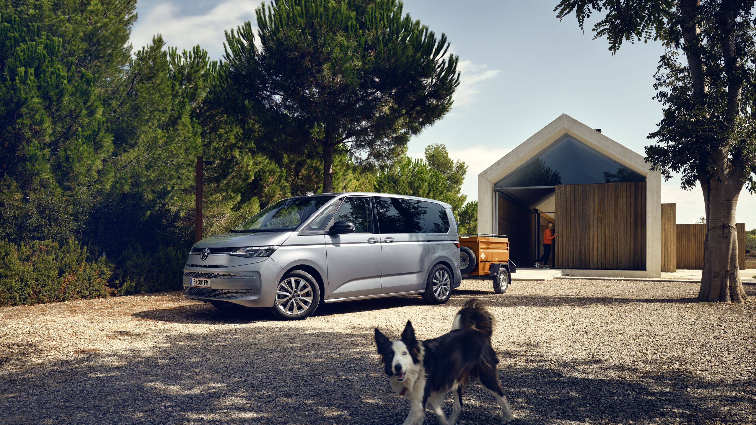 Ein Hund läuft vor einem neuen VW Multivan T7 2021 mit Anhänger.