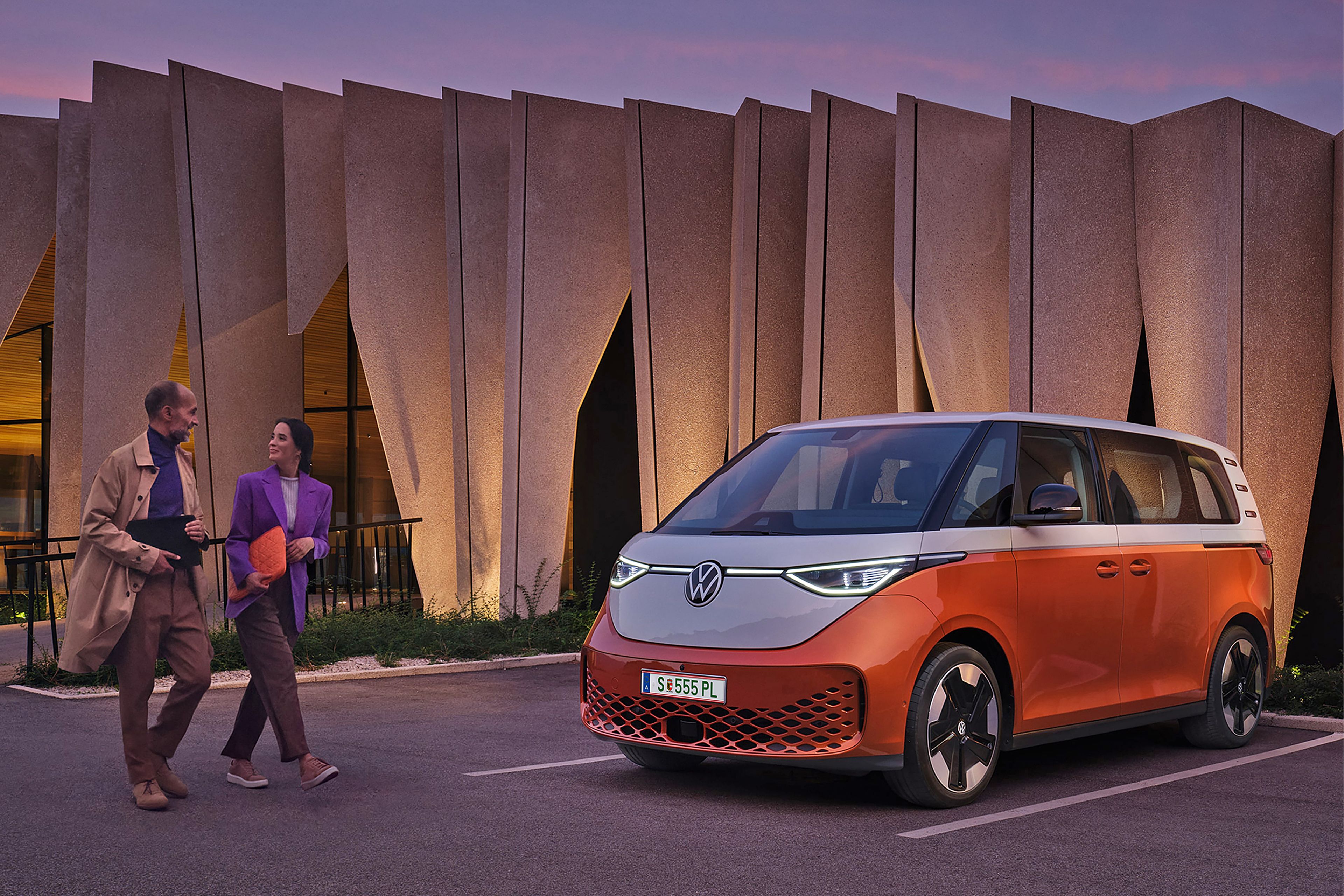 Двойка пред модерен сграден силует с паркиран електрически Volkswagen ID. Buzz