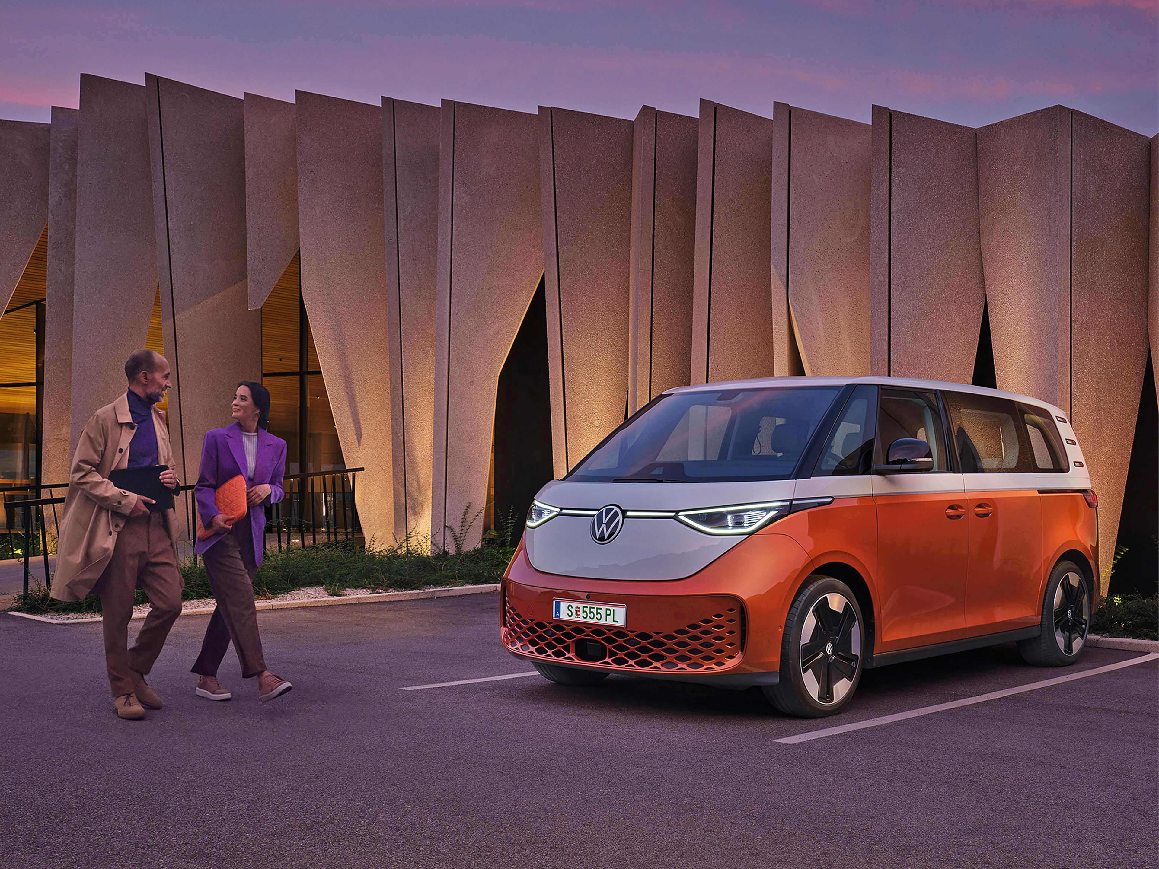 Двойка пред модерен сграден силует с паркиран електрически Volkswagen ID. Buzz