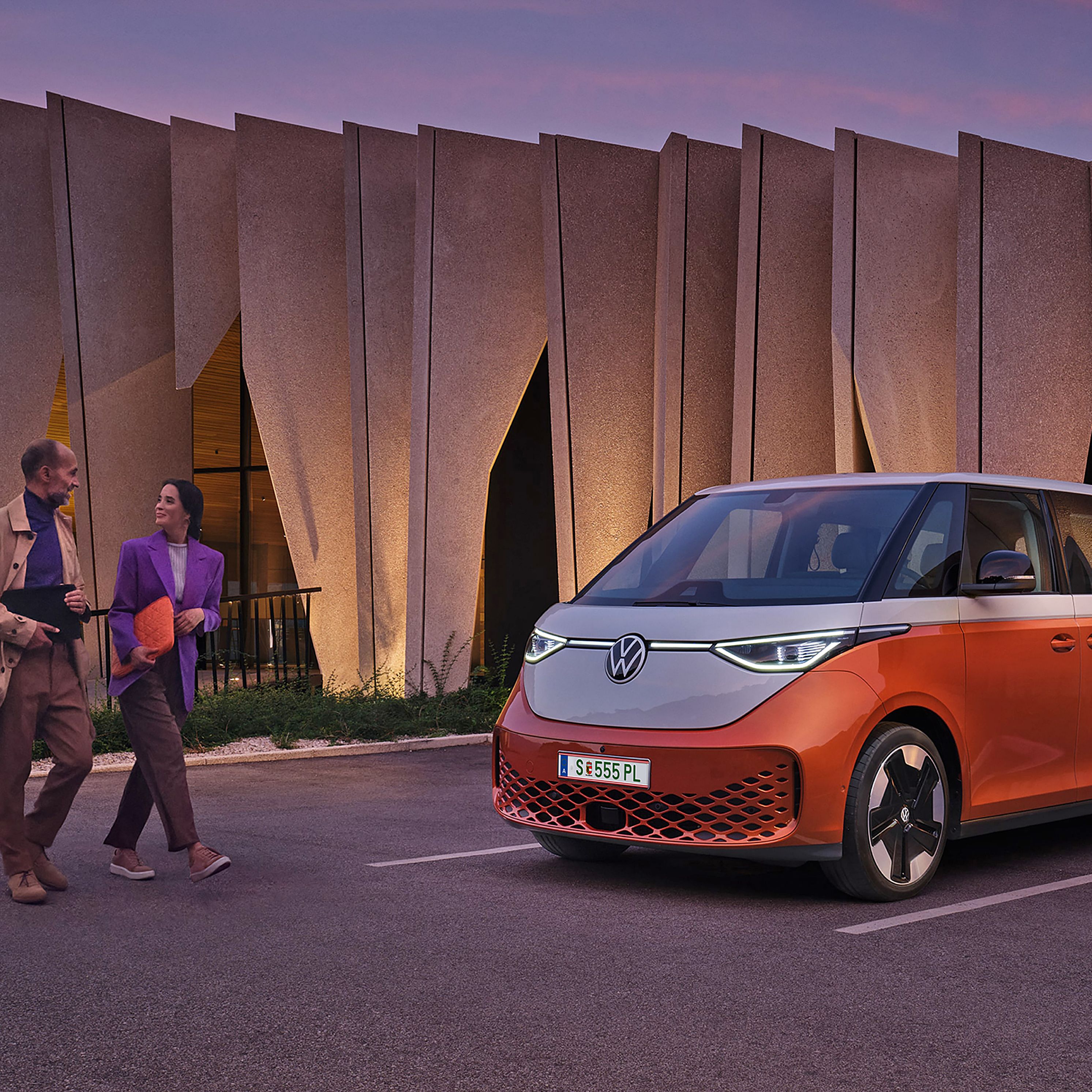 Двойка пред модерен сграден силует с паркиран електрически Volkswagen ID. Buzz