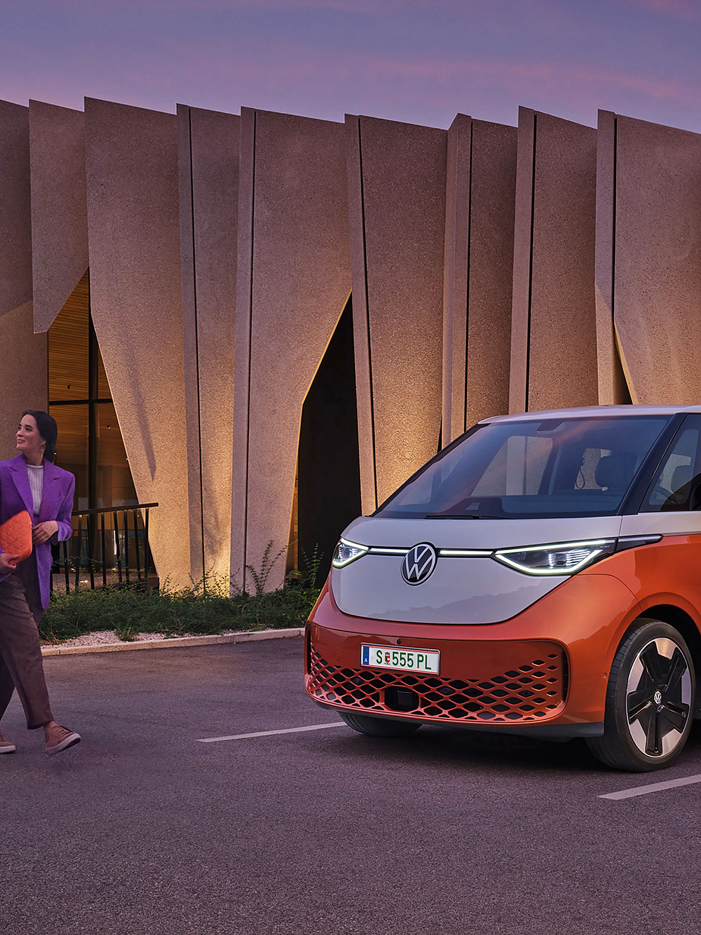 Двойка пред модерен сграден силует с паркиран електрически Volkswagen ID. Buzz