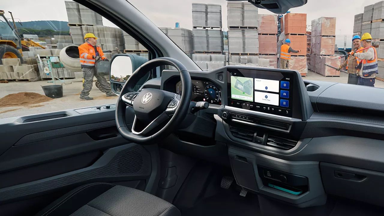 Вътрешен изглед на Volkswagen Transporter с дигитален дисплей и работници на строителна площадка отвън.