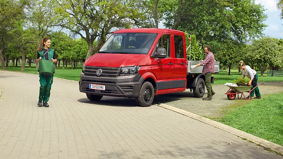 Червен Volkswagen Crafter със самосвал, използван от екип озеленители в парк