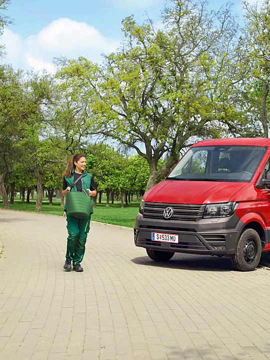 Червен Volkswagen Crafter със самосвал, използван от екип озеленители в парк