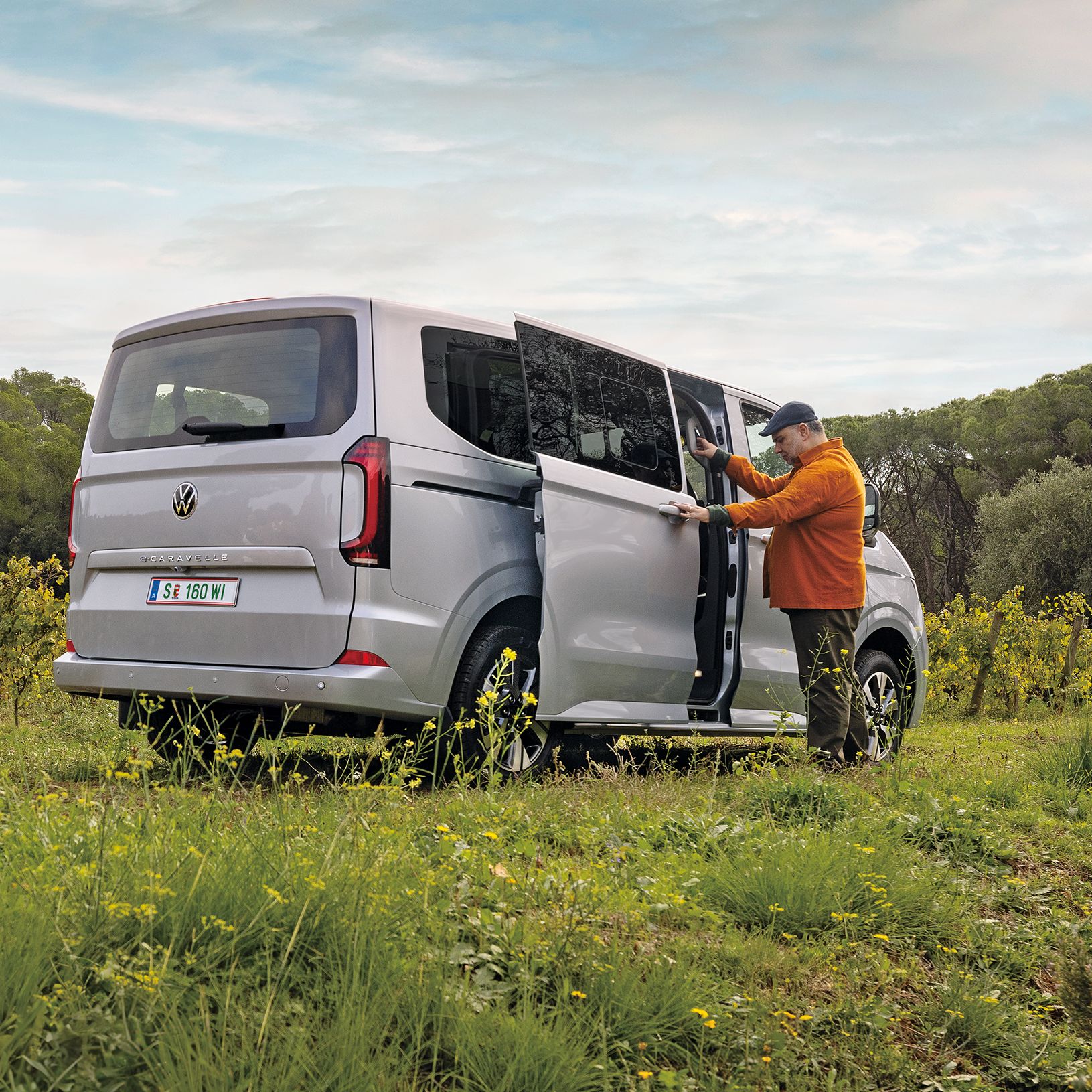 Група приятели до Volkswagen Caravelle, паркиран сред зелени поляни и дървета