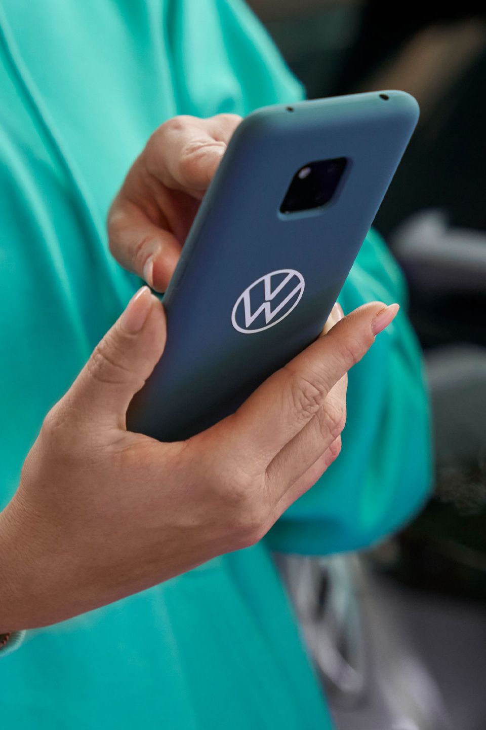 Eine Frau tippt in ihr Smartphone. Auf der blauen Schutzhülle ist das Volkswagen Logo abgebildet.