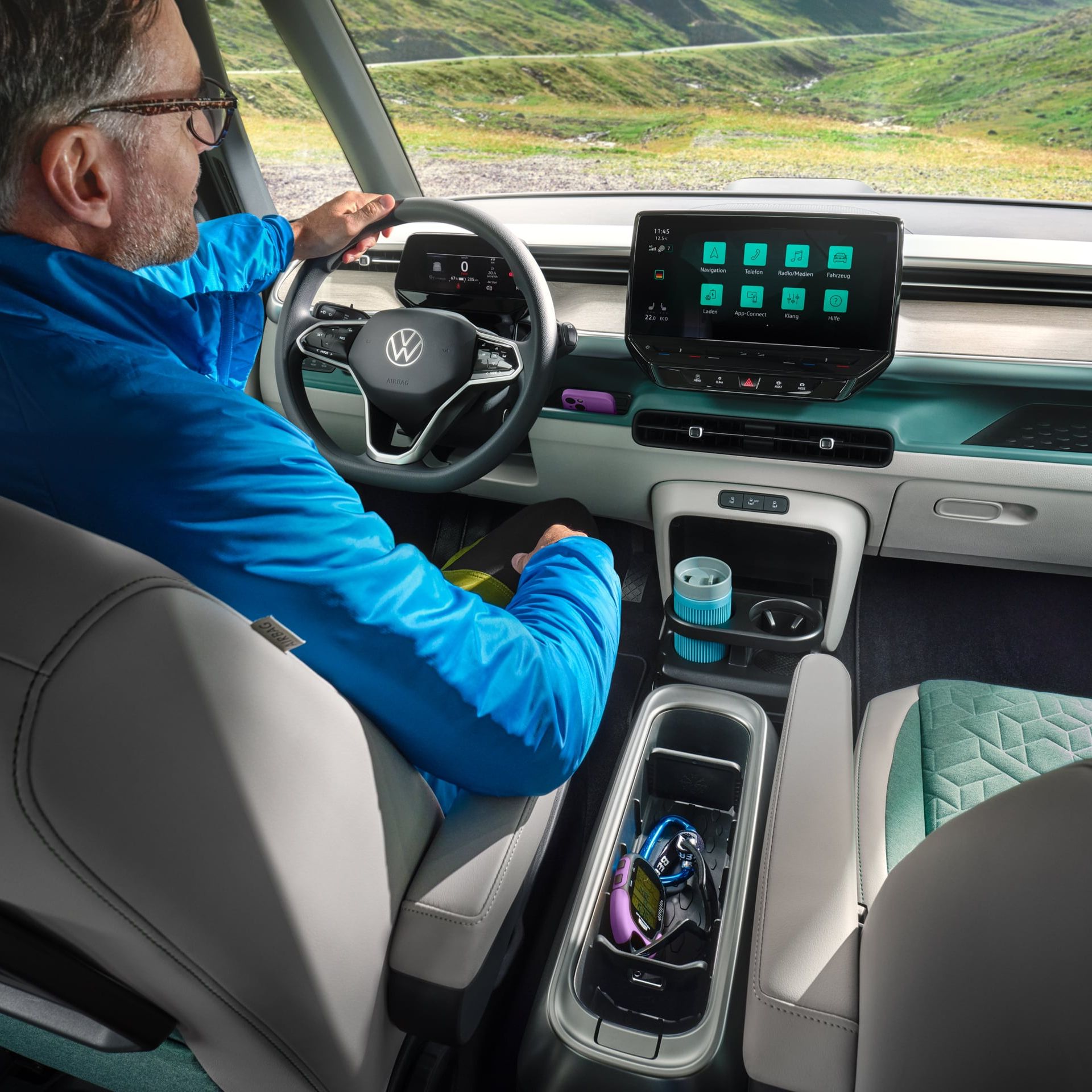 Интериор на Volkswagen ID. Buzz с водач и дигитален кокпит, подлакътник с поставка за вещи и изглед към планински пейзаж