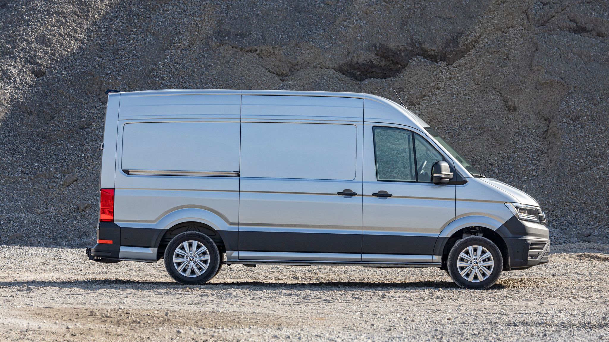 Страничен изглед на сребрист Volkswagen Crafter, паркиран на фонов терен с чакъл.