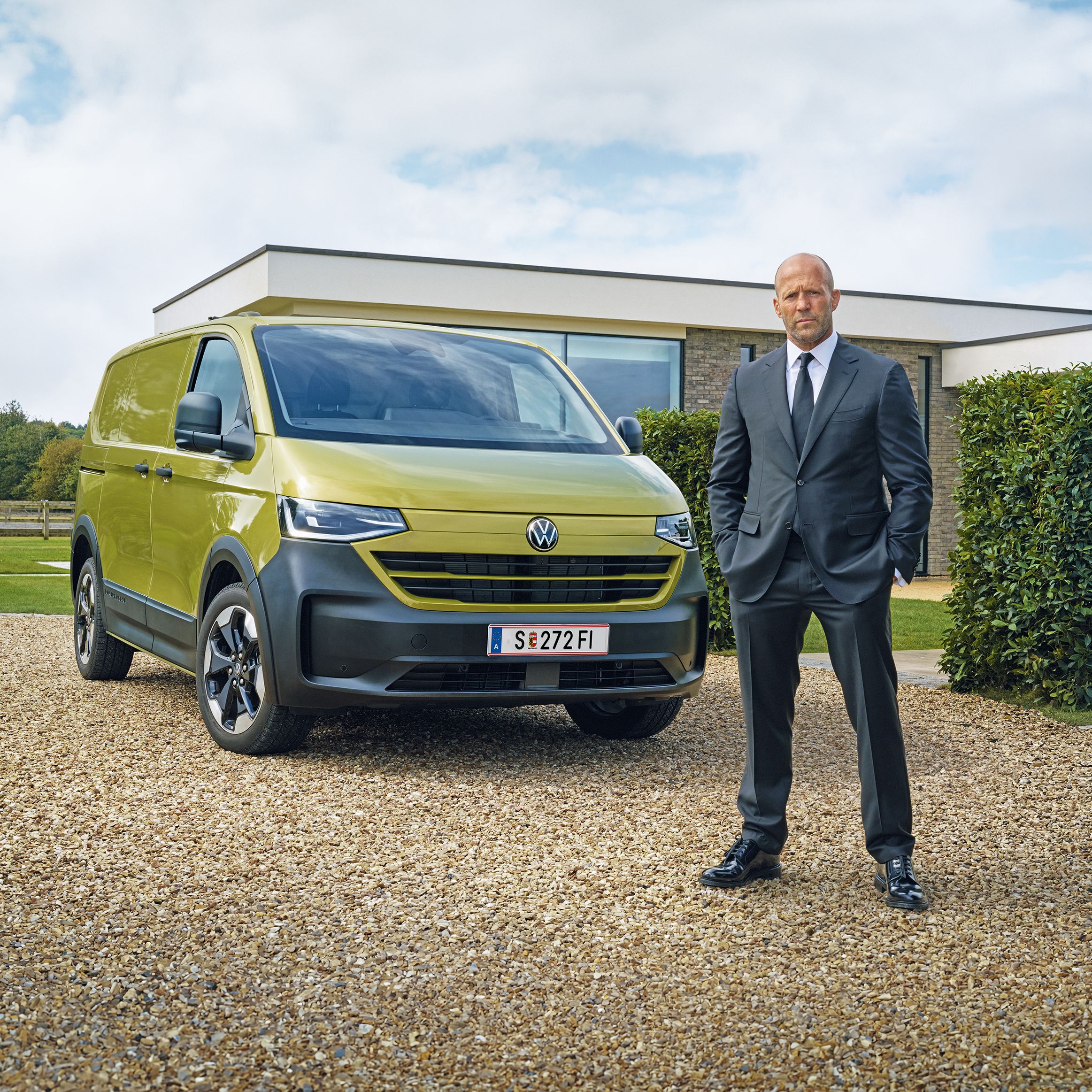 Мъж в елегантен костюм пред новия Volkswagen Transporter в лимонено-зелен цвят, паркиран пред модерна къща
