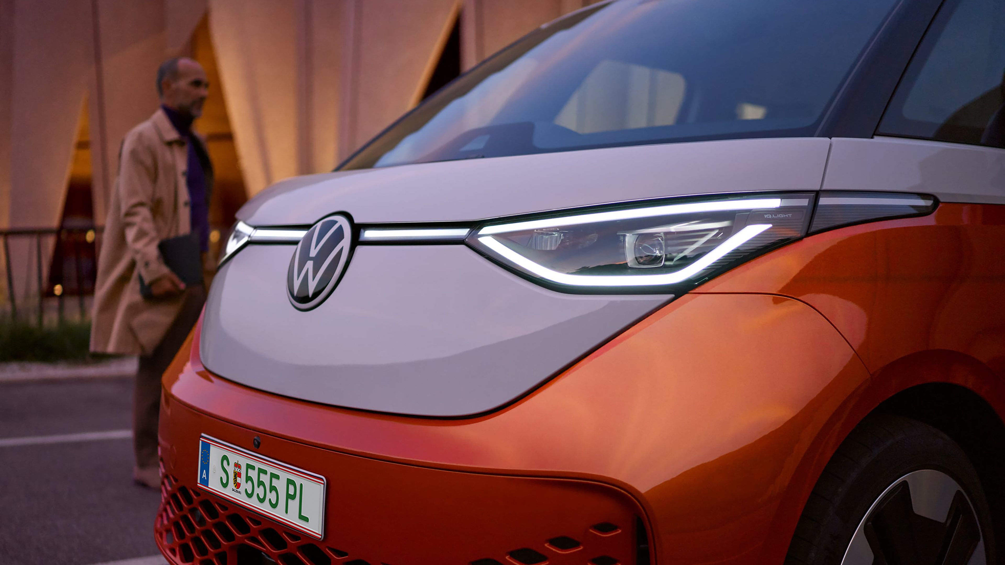 Оранжево-бял Volkswagen ID. Buzz с включени IQ.LIGHT светлини на здрач.