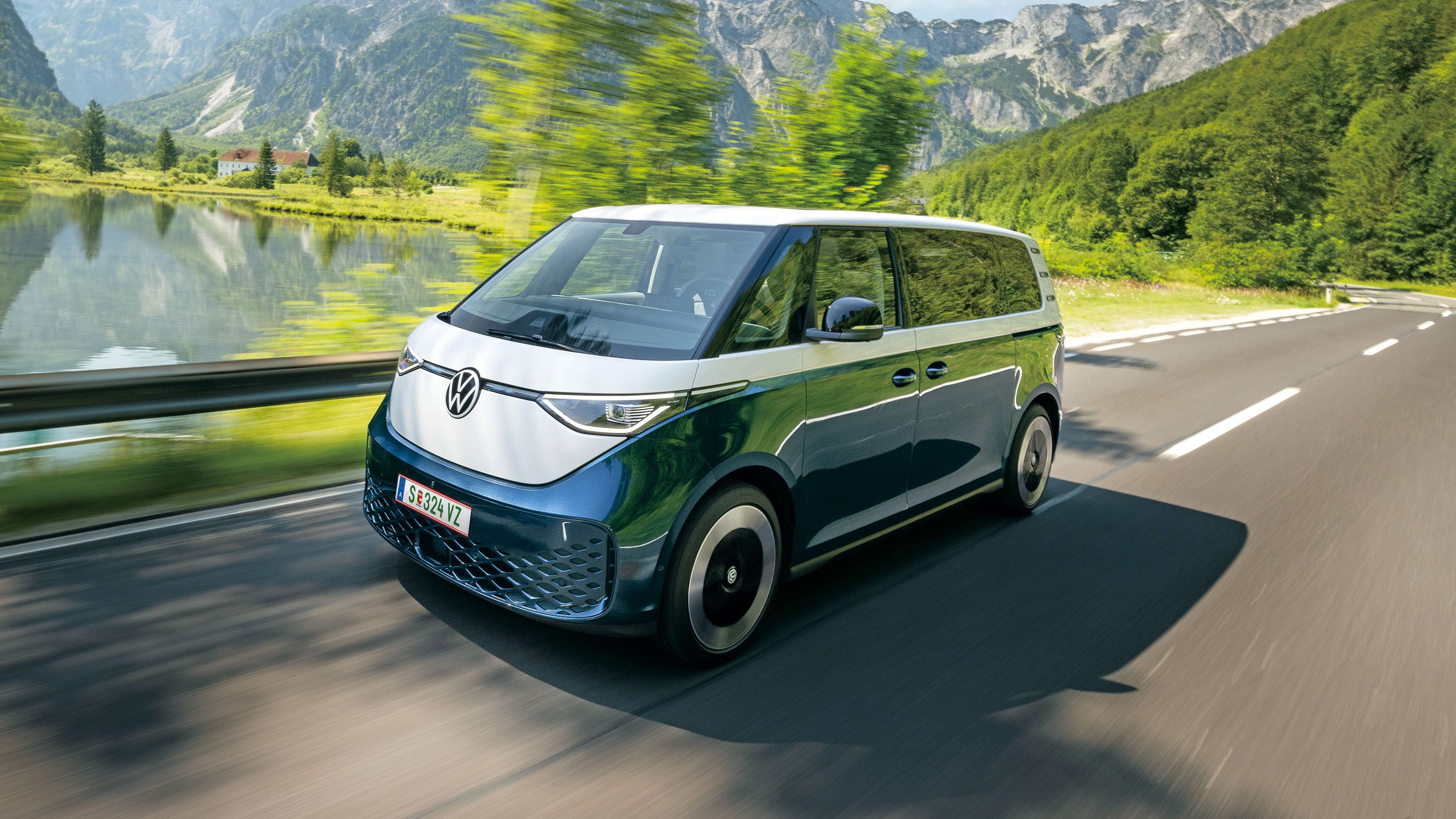 Електрическият Volkswagen ID. Buzz в движение сред живописен планински пейзаж с езеро и скалисти върхове.