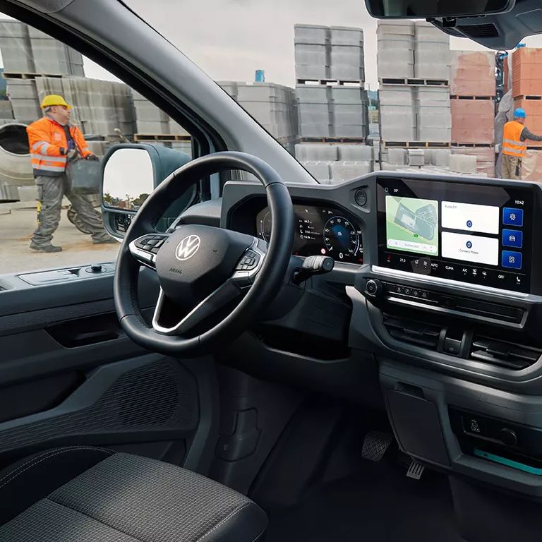 Вътрешен изглед на Volkswagen Transporter с дигитален дисплей и работници на строителна площадка отвън.