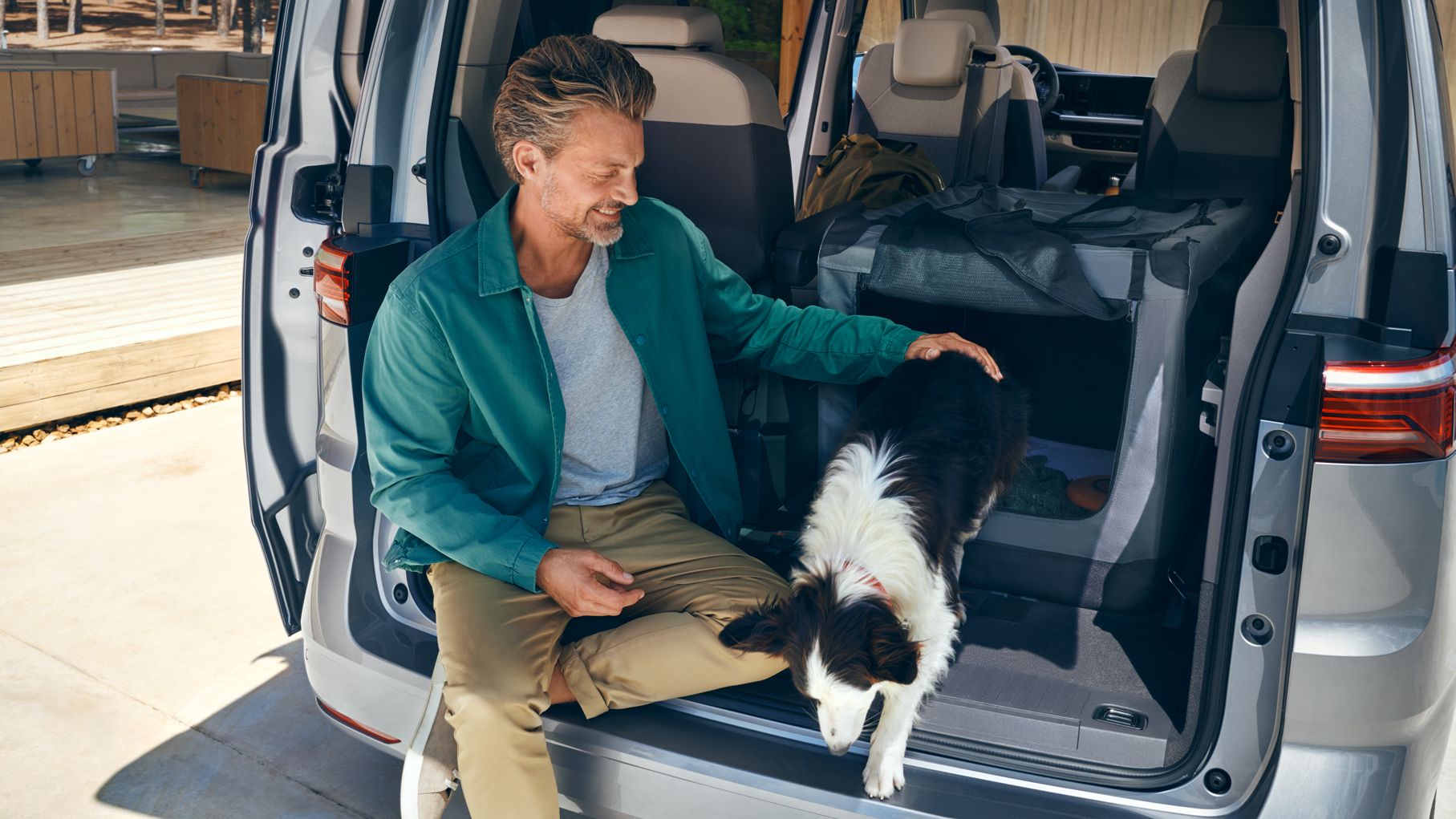 Ein Mann sitzt mit einem Hund im Kofferraum des neuen VW Multivan Life T7 2021.