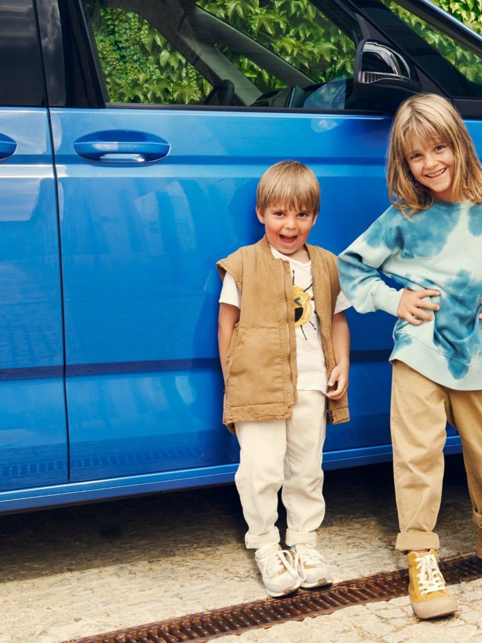 Drei Kinder stehen vor einem blauen neuen VW Multivan T7 2021.