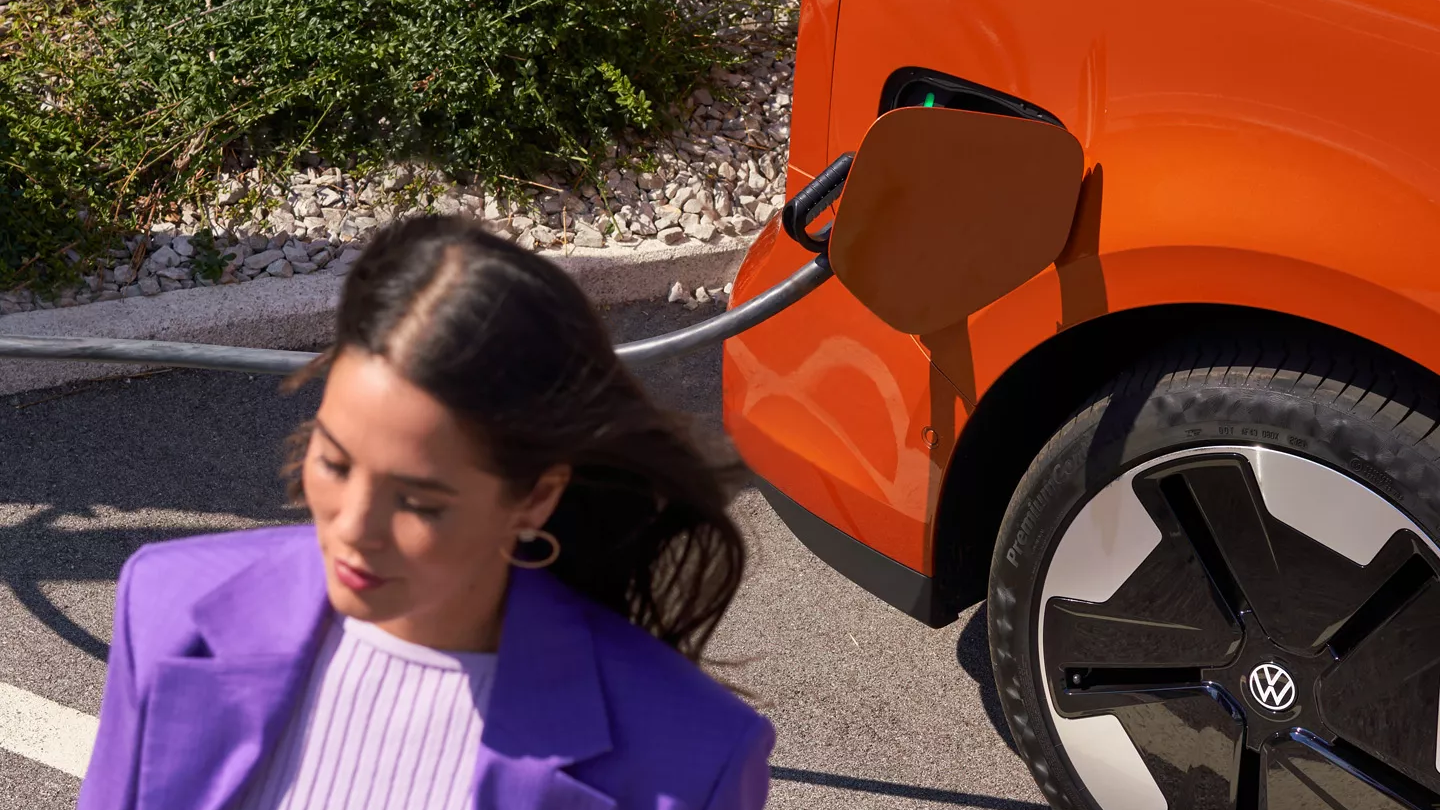 Жена до зареждащ се електрически Volkswagen ID. Buzz в оранжев цвят