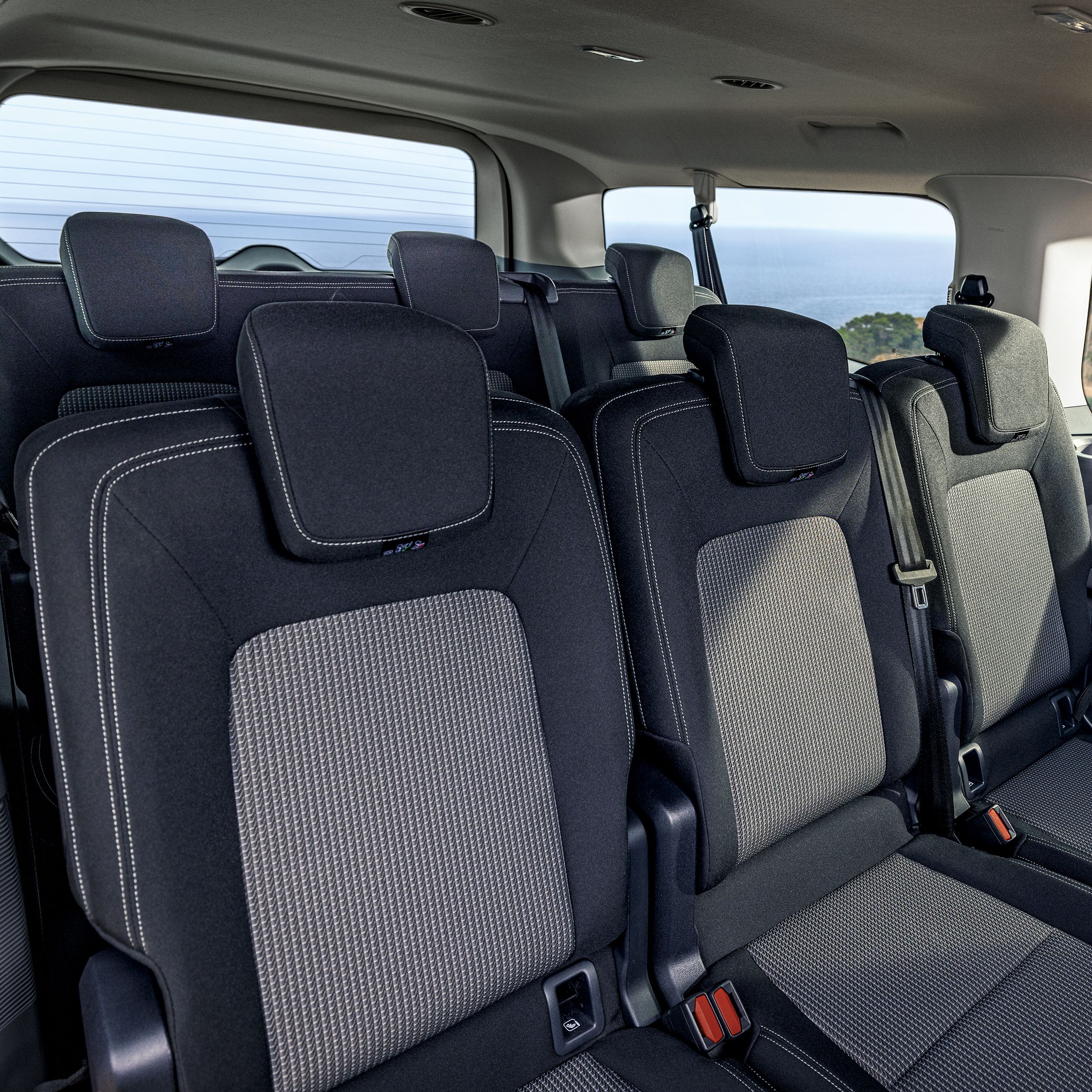 Интериор на Volkswagen Caravelle с три реда седалки и изглед към колоездачи през прозореца