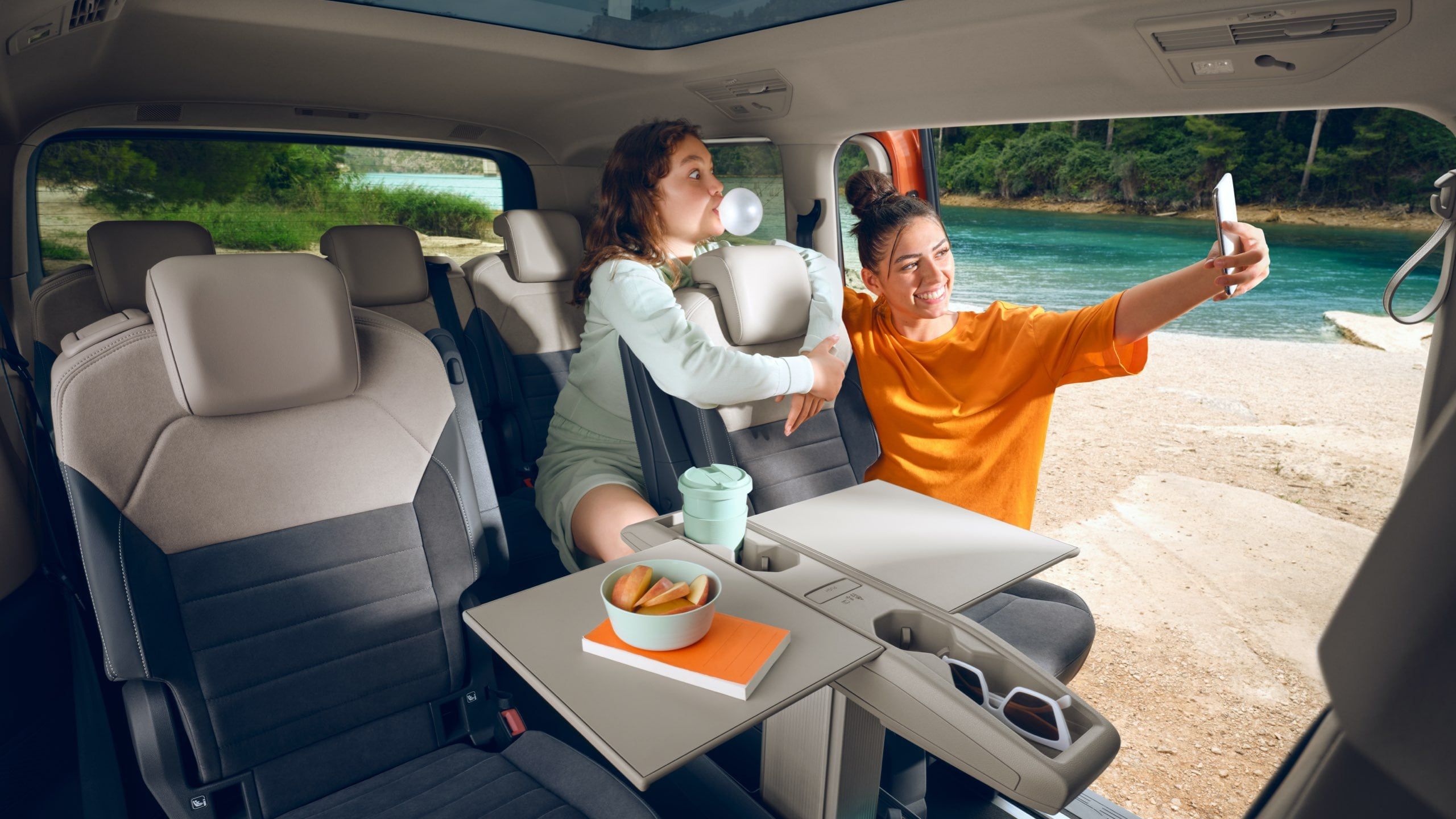 Zwei Teenager machen Bilder im neuen VW Multivan T7 2021 Energetic mit Multifunktionstisch.