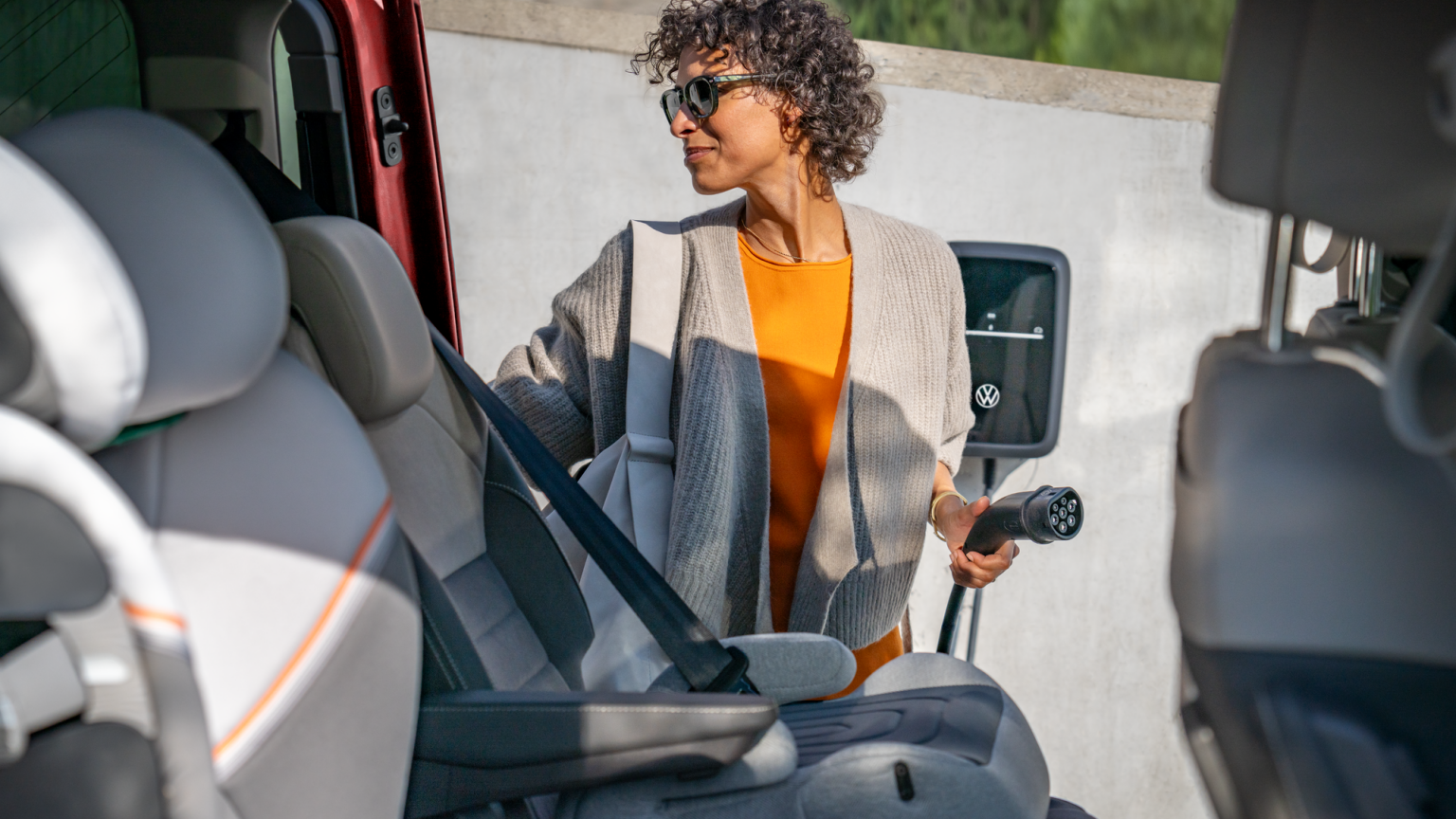 Blick aus dem Inneren eines Volkswagen Multivan. Zu sehen ist eine Frau mit einem Ladekabel und einer Wallbox.