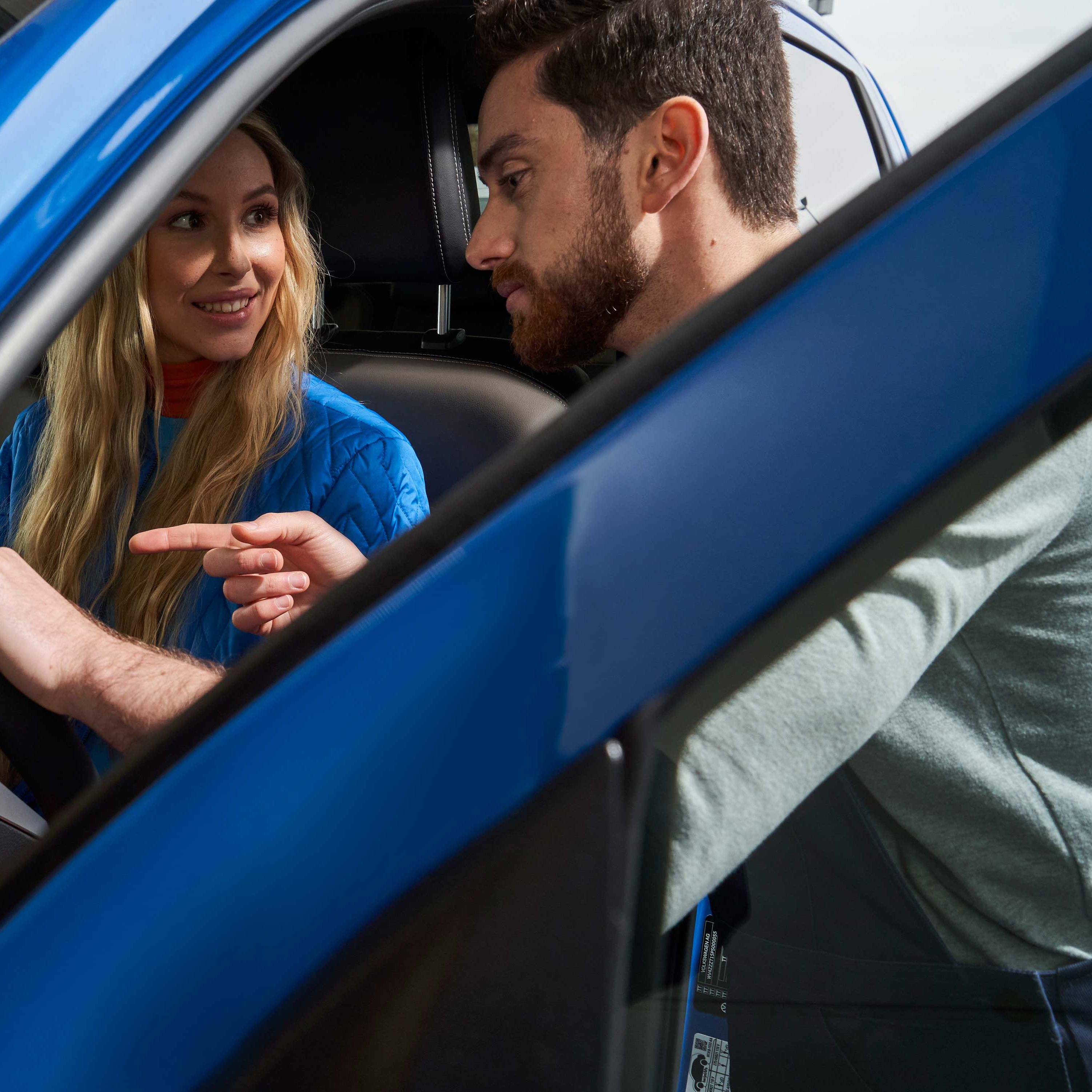 Ein Volkswagen Service Techniker spricht mit einer Kundin, die in einem Volkswagen sitzt