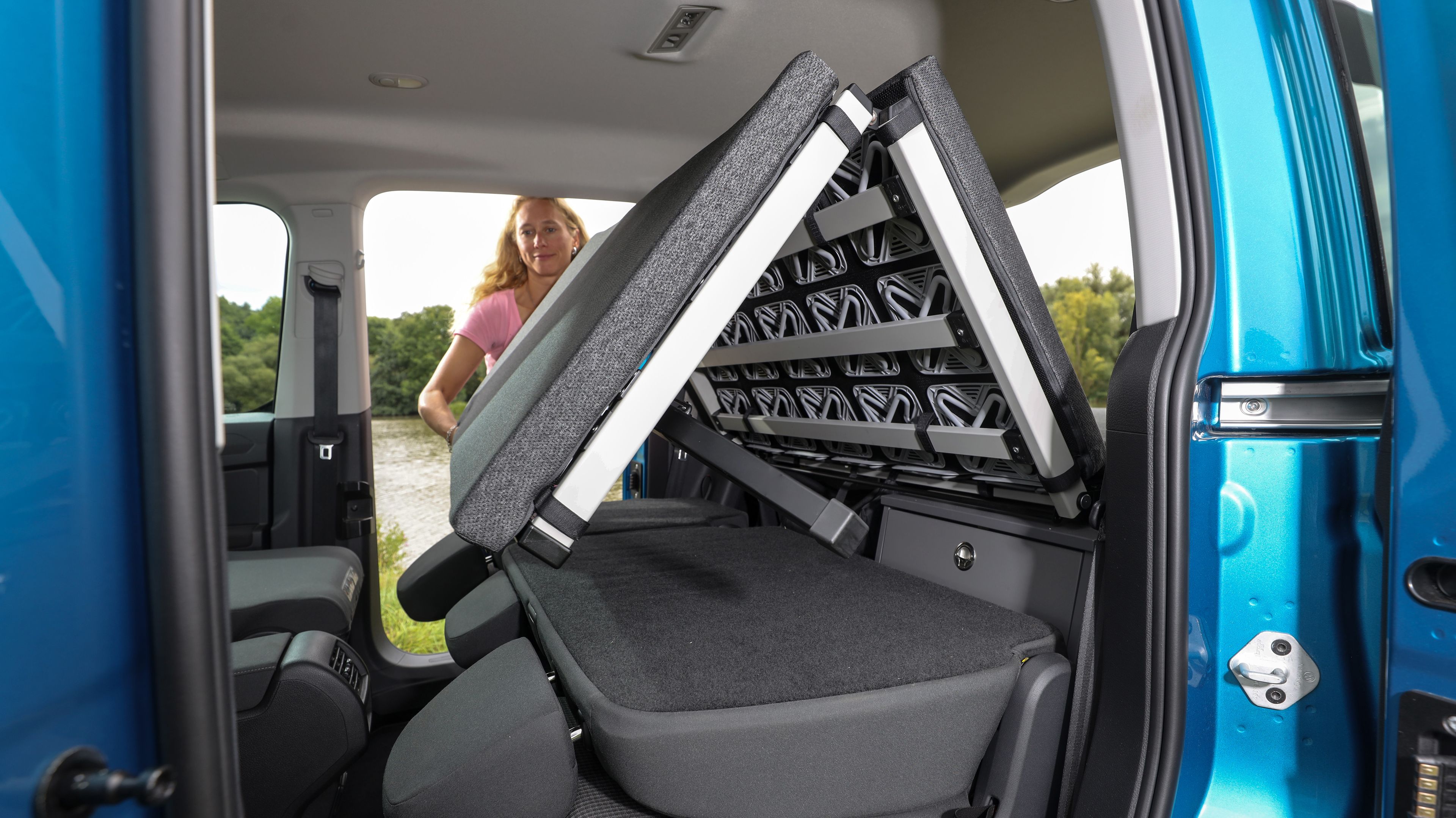 Frau klappt Bett von VW Caddy California zusammen.
