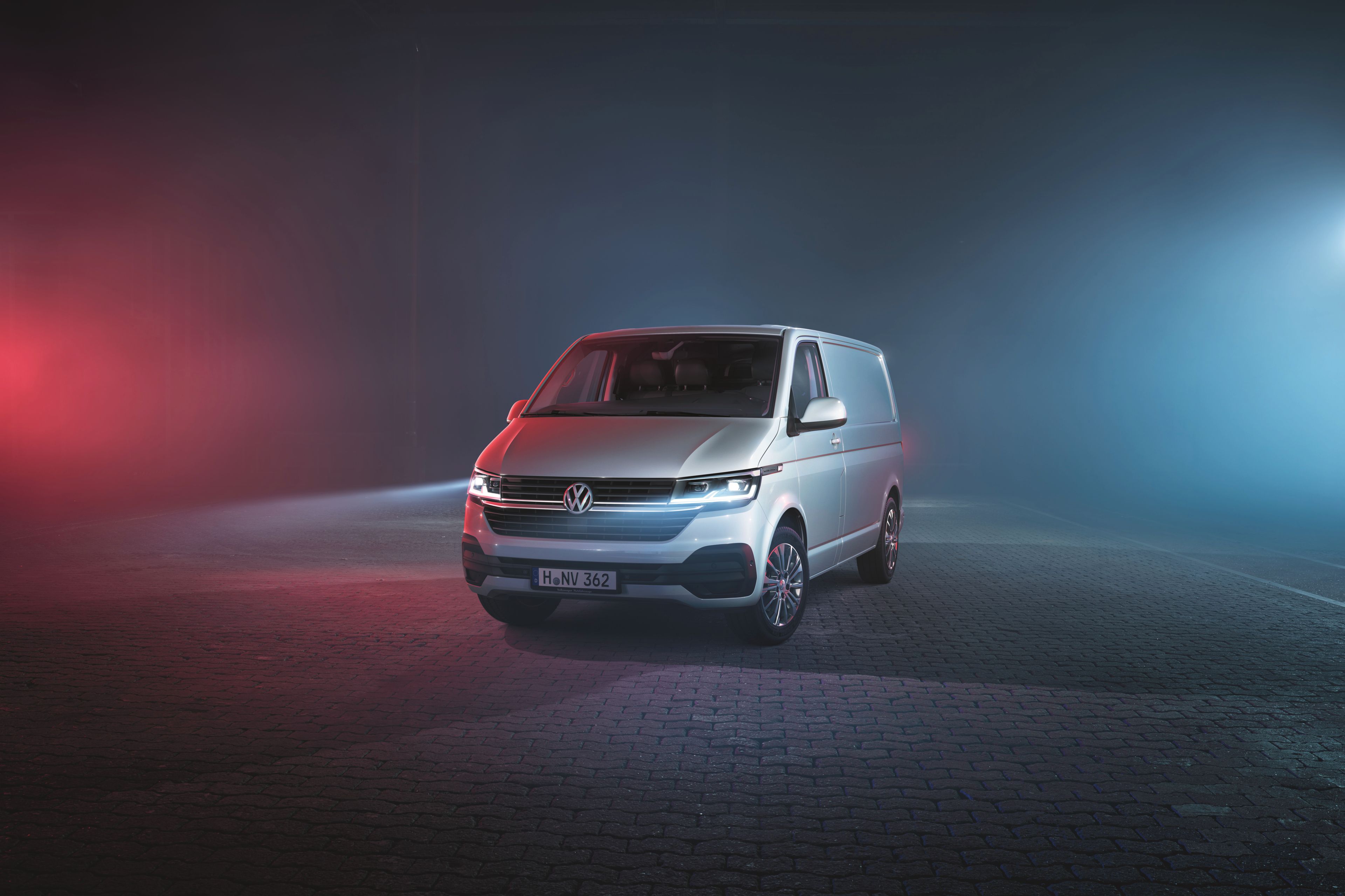 Сребрист Volkswagen Transporter, заснет отпред в нощна атмосфера с цветно осветление.