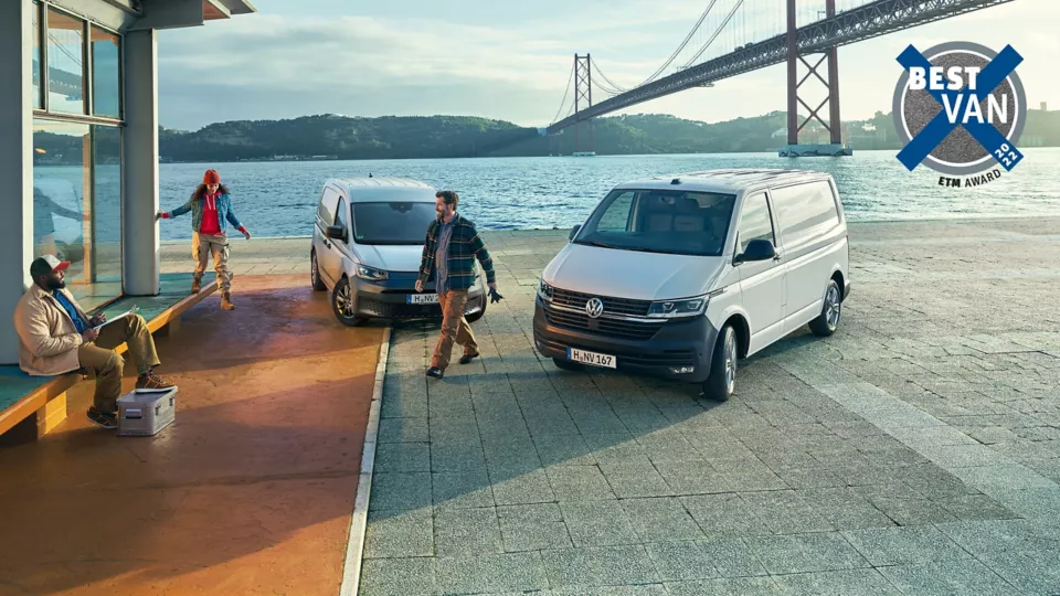 Два товарни автомобила Volkswagen – Caddy и Transporter – паркирани край морето до мост, с работници в работна среда; лого „Best Van 2022“ в горния десен ъгъл.
