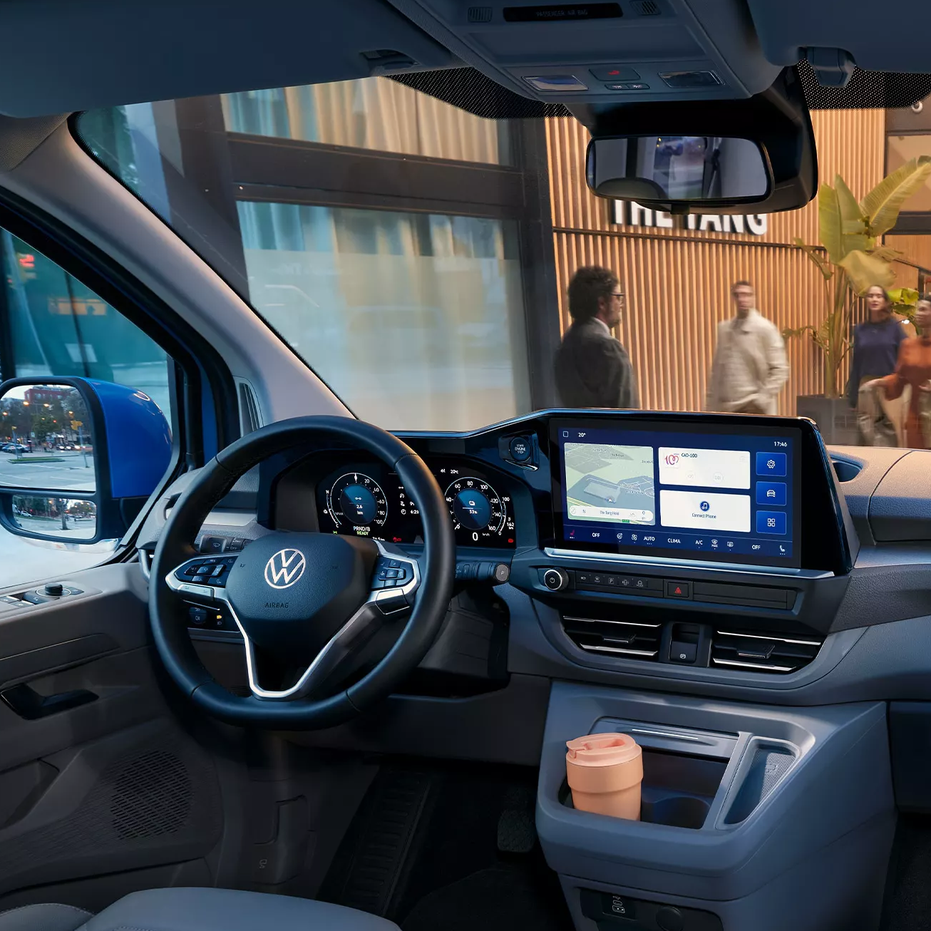 Интериор на Volkswagen Caravelle с модерен кокпит и дигитален дисплей, паркиран пред хотел