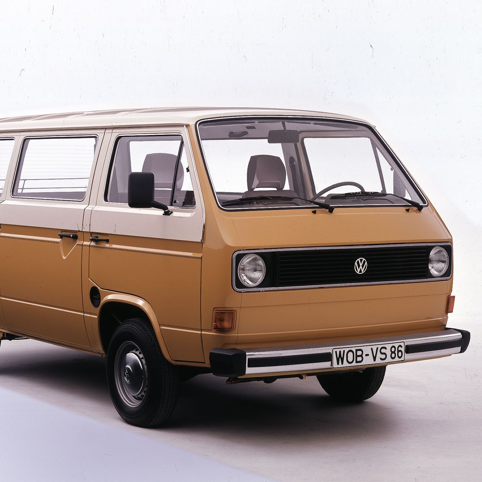 Класически ван, модел Volkswagen Transporter от 1970-те или 1980-те години, боядисан в жълто-кафяв цвят. Ванът има големи странични прозорци и бяла табела с регистрация.