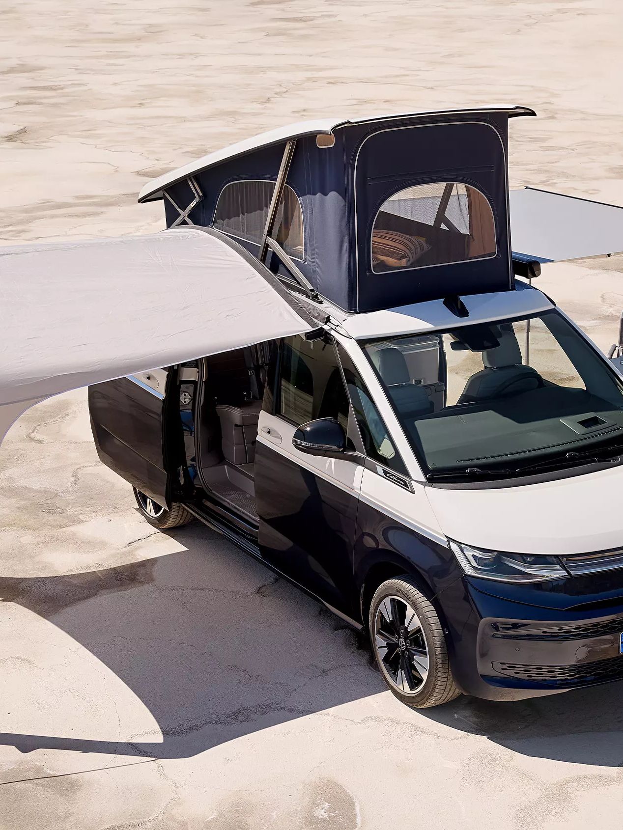 Кемпер Volkswagen California Ocean с разпъната тента и повдигнат покрив, готов за къмпинг.