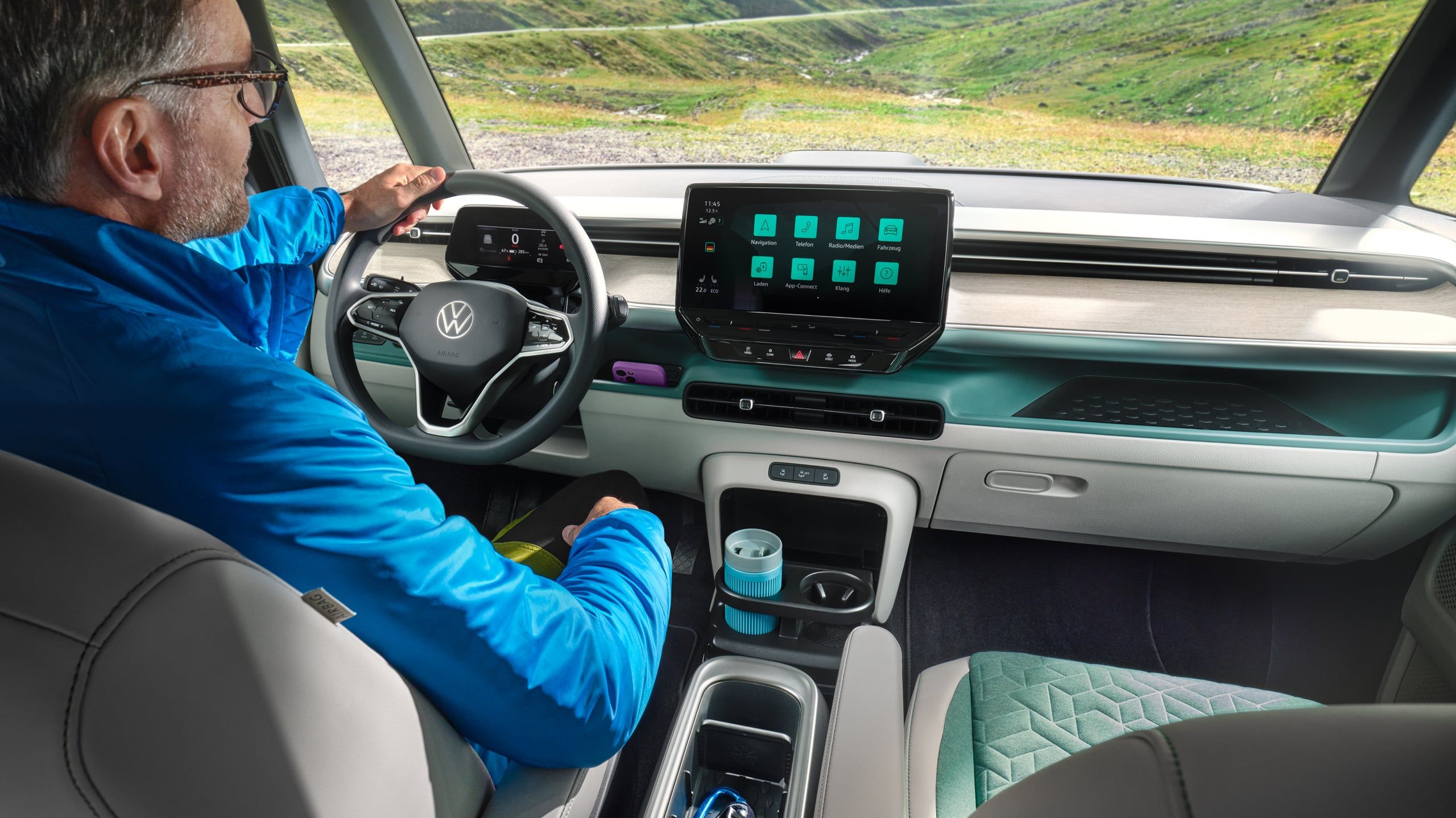 Интериор на Volkswagen ID. Buzz с водач и дигитален кокпит, подлакътник с поставка за вещи и изглед към планински пейзаж