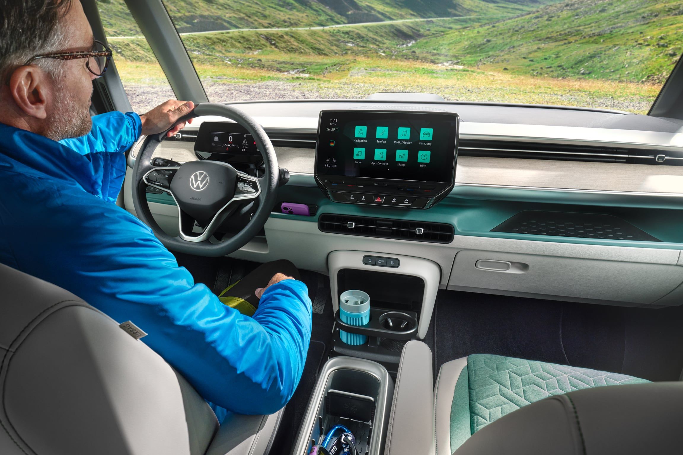 Интериор на Volkswagen ID. Buzz с водач и дигитален кокпит, подлакътник с поставка за вещи и изглед към планински пейзаж