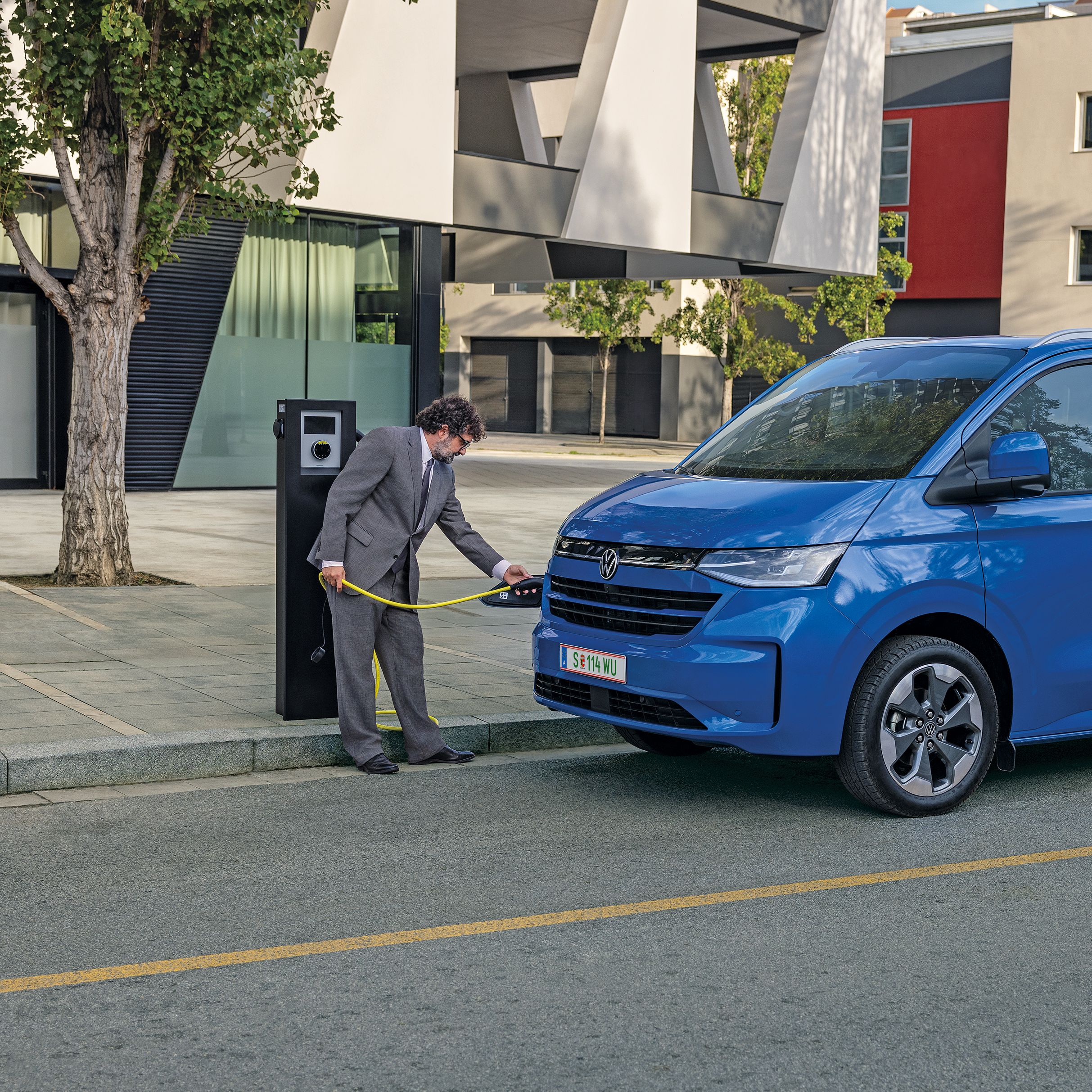 Мъж зарежда електрически Volkswagen Transporter, докато пътничка се качва в задната част на вана