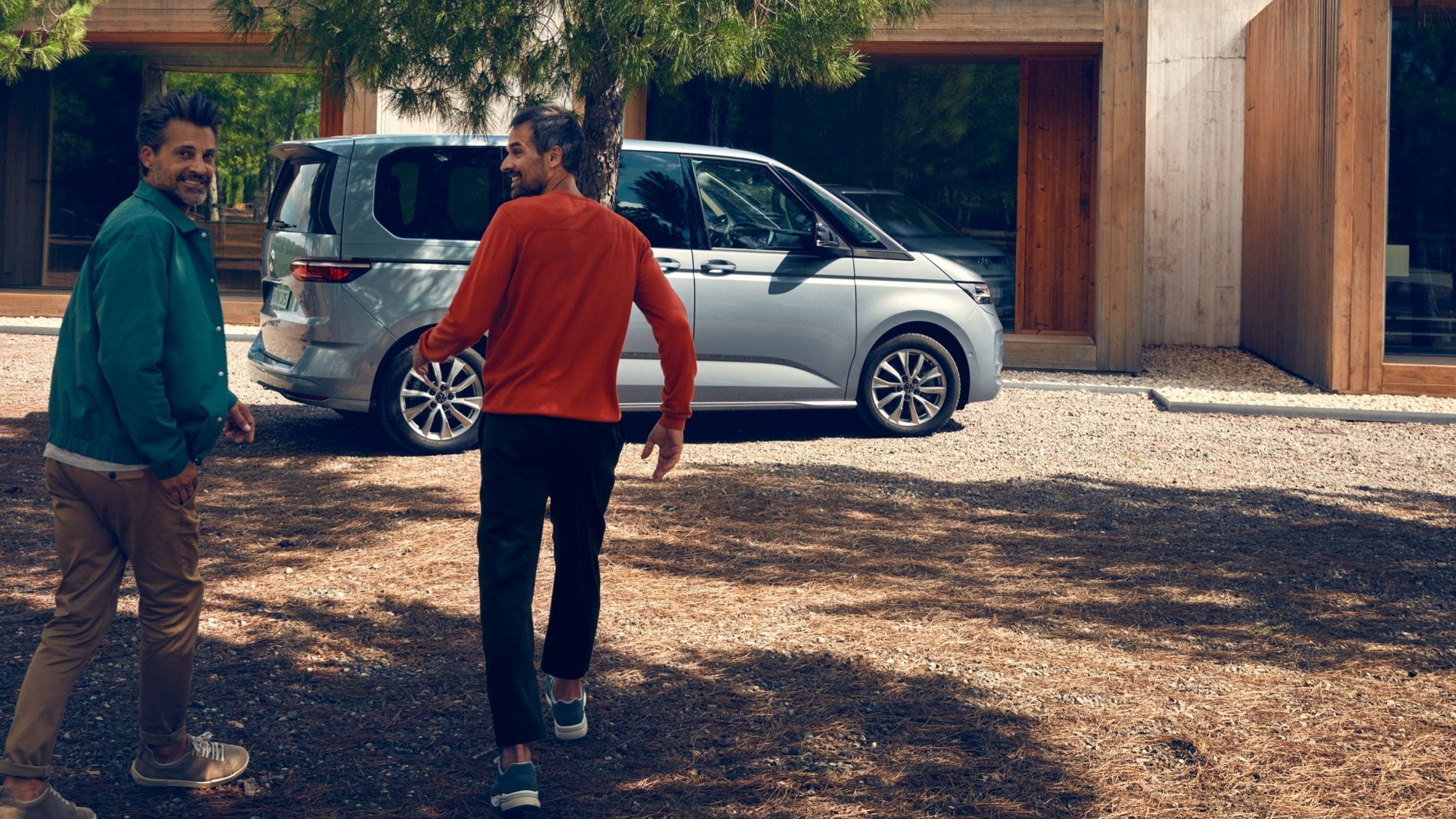 Zwei Männer laufen auf einen silbernen neuen VW Multivan T7 2021 zu.