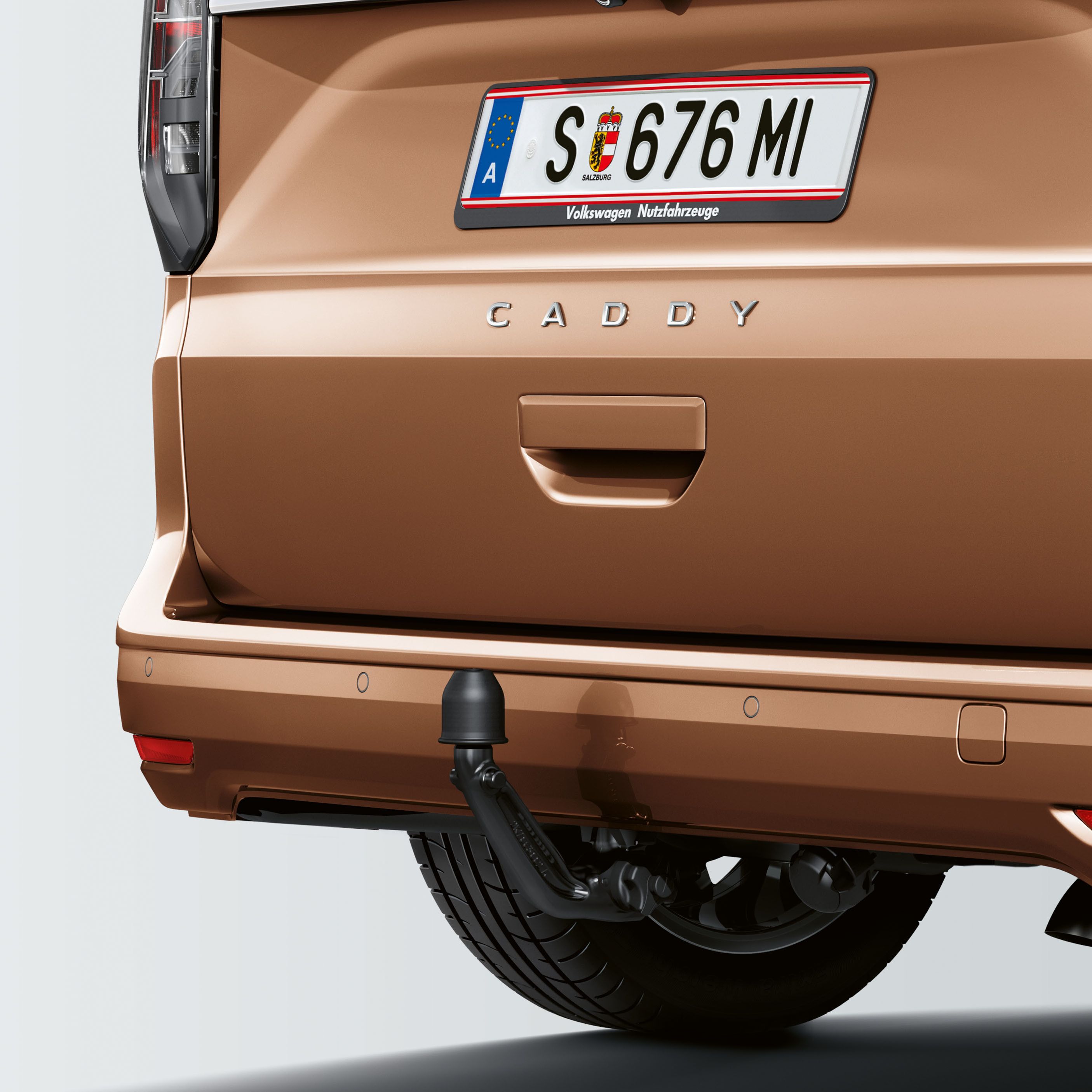 Задната част на кафяв автомобил с австрийска регистрационна табела SE 676 MI и надпис CADDY. Автомобилът е оборудван с теглич.