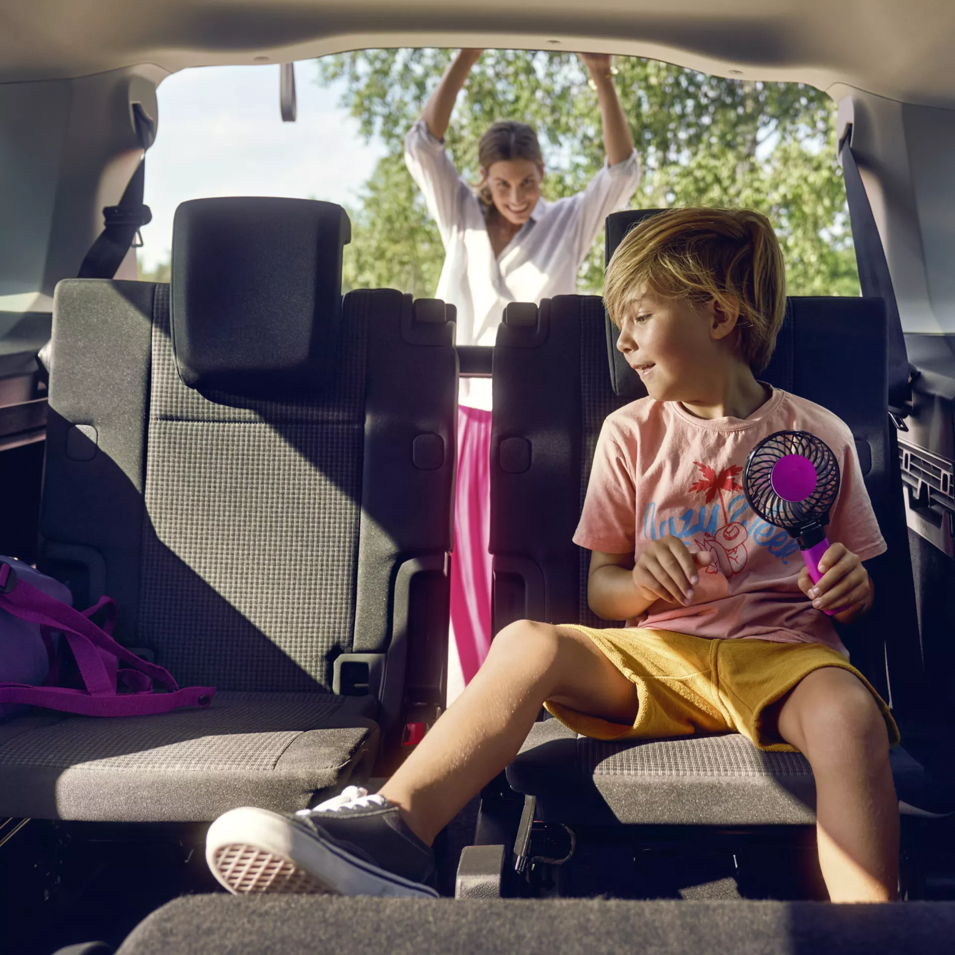 Детето седи на задната седалка на Caddy, майката затваря задната врата 