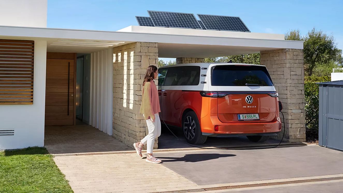 Жена пред модерен дом с електрически Volkswagen ID. Buzz, който се зарежда от соларна система