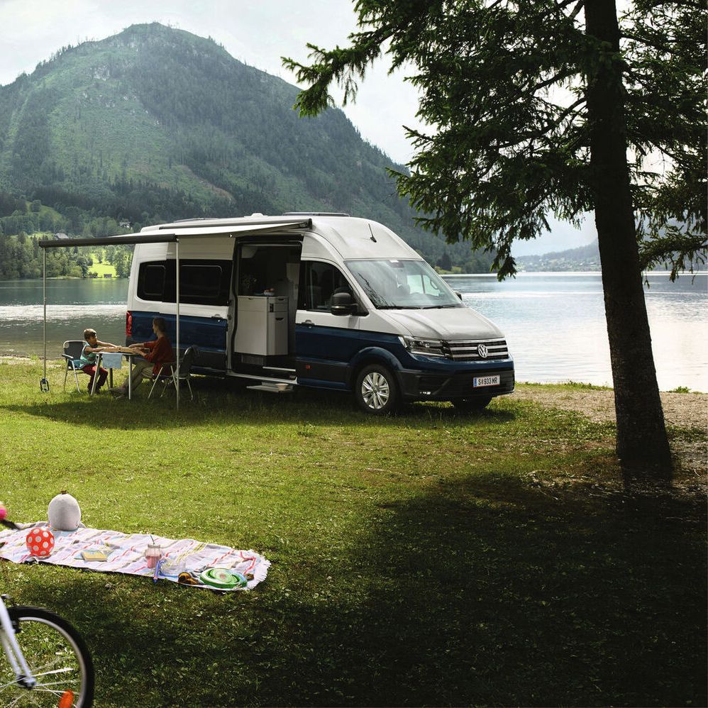 Семейна почивка с два кемпера Volkswagen край езеро в планината, деца играят на поляната.