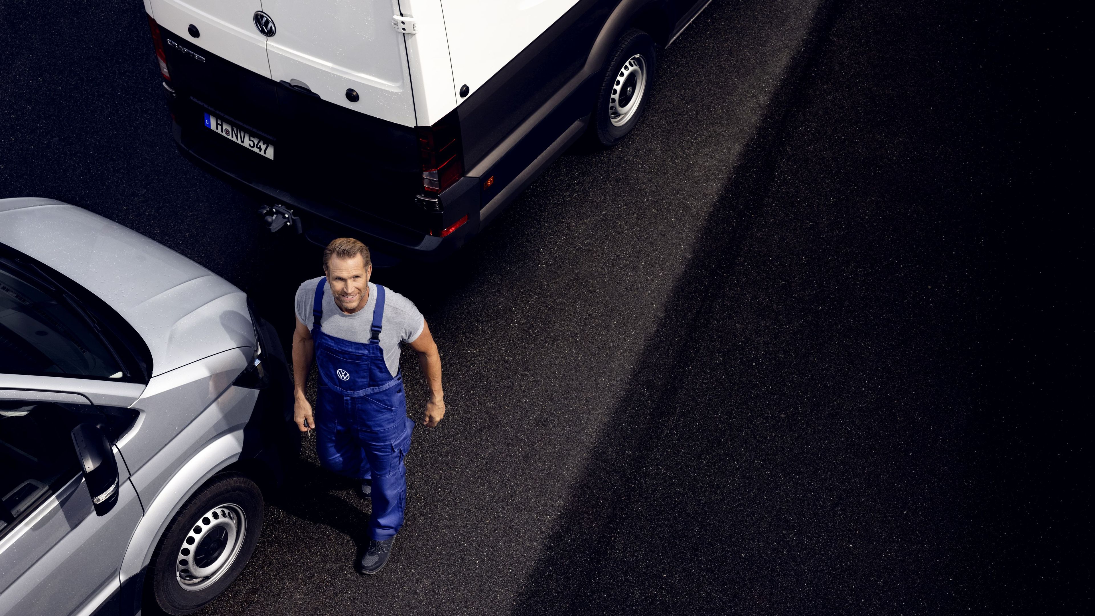 Мъж в работен гащеризон Volkswagen стои между два сиви товарни автомобила
