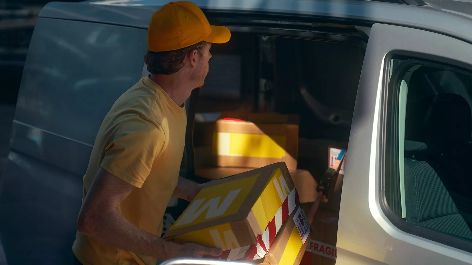 Куриер в жълта униформа товари пакети в страничната врата на сребрист товарен автомобил Volkswagen.