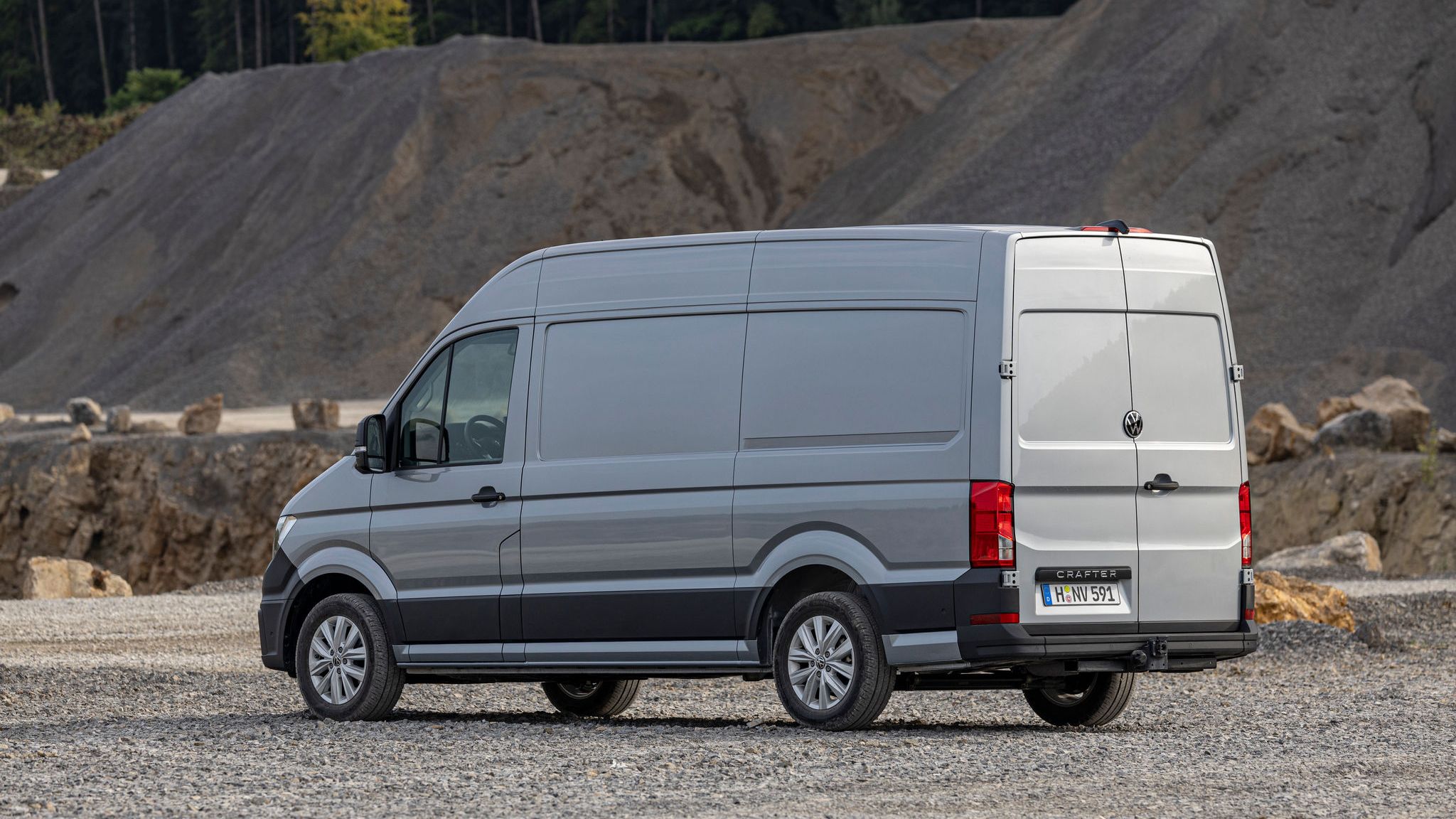 Сив товарен ван Volkswagen Crafter, паркиран в индустриална зона с чакъл и камъни.