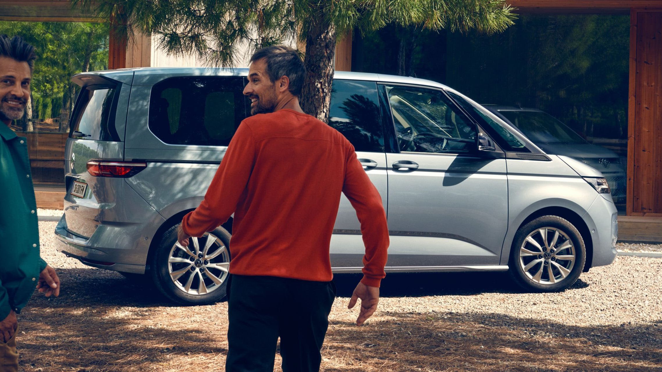 Zwei Männer laufen lachend auf den neuen VW Multivan Life T7 2021 zu.