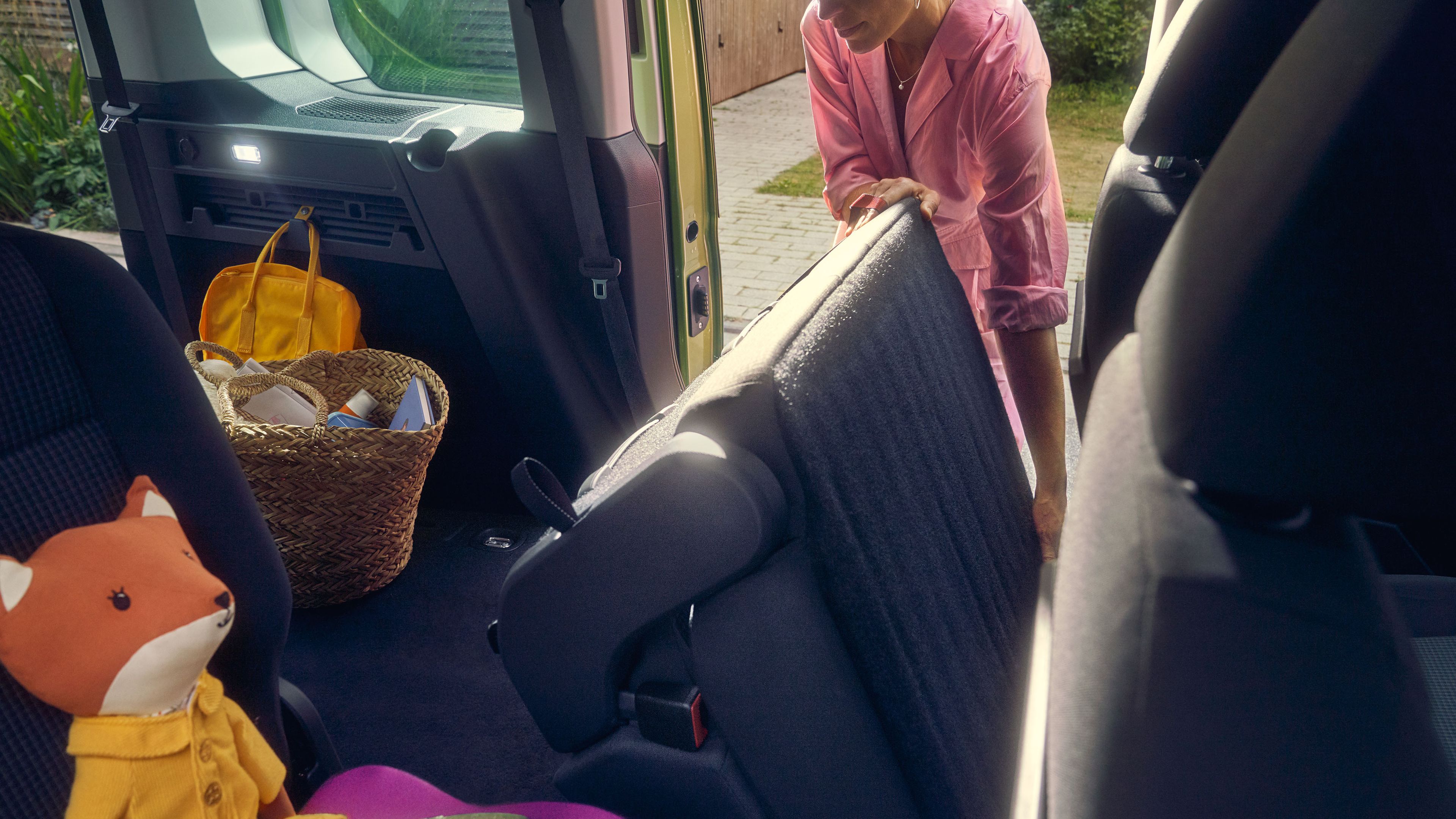 Жена сгъва седалка в задната част на Volkswagen, а в колата има детска играчка лисица и кошница с вещи